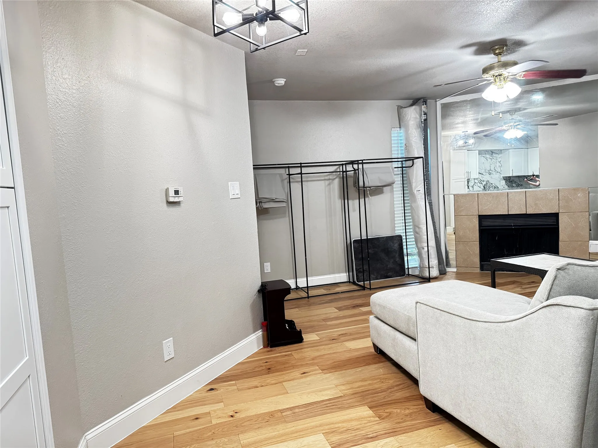 Living area featuring wood-finish flooring, a tiled fireplace with a dark firebox, and a ceiling fan