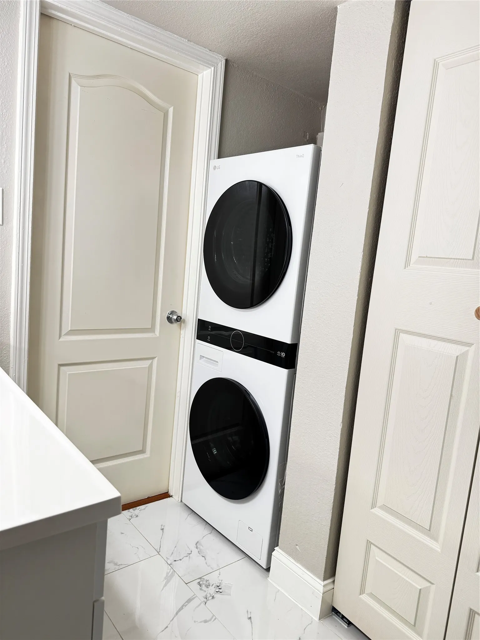 White stacked washer and dryer unit, set on white marble-look floor tiles