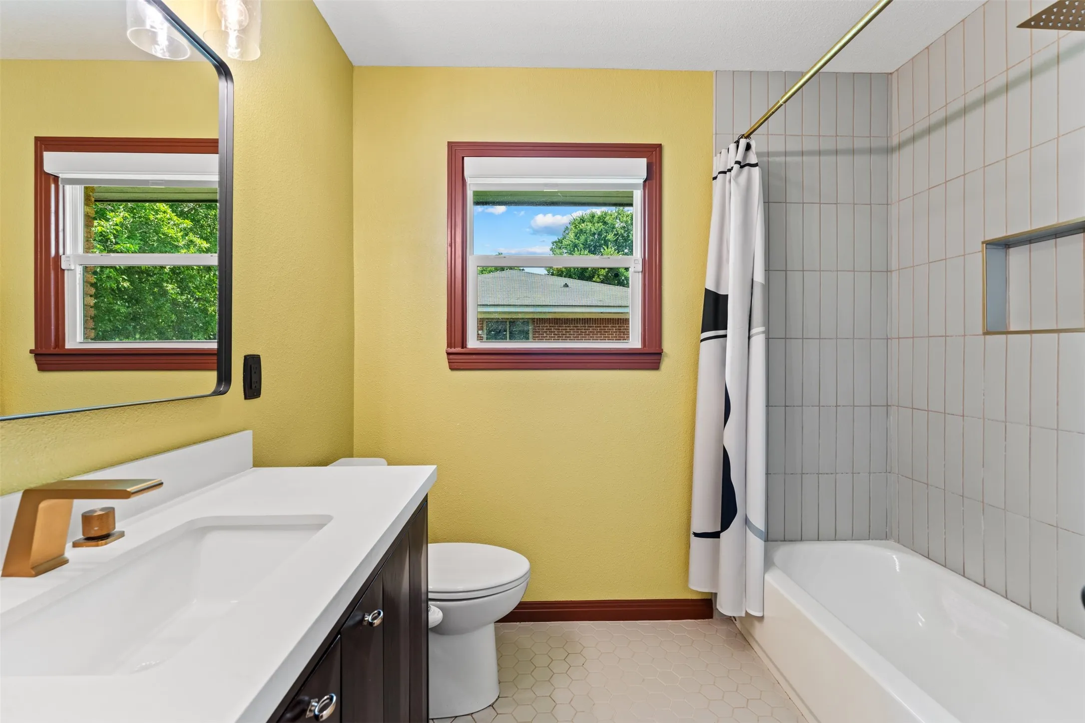 Bathroom featuring a single vanity with a white countertop and bronze-toned faucet, a built-in bathtub with subway tile surround, a recessed shower niche, and hexagonal floor tiling