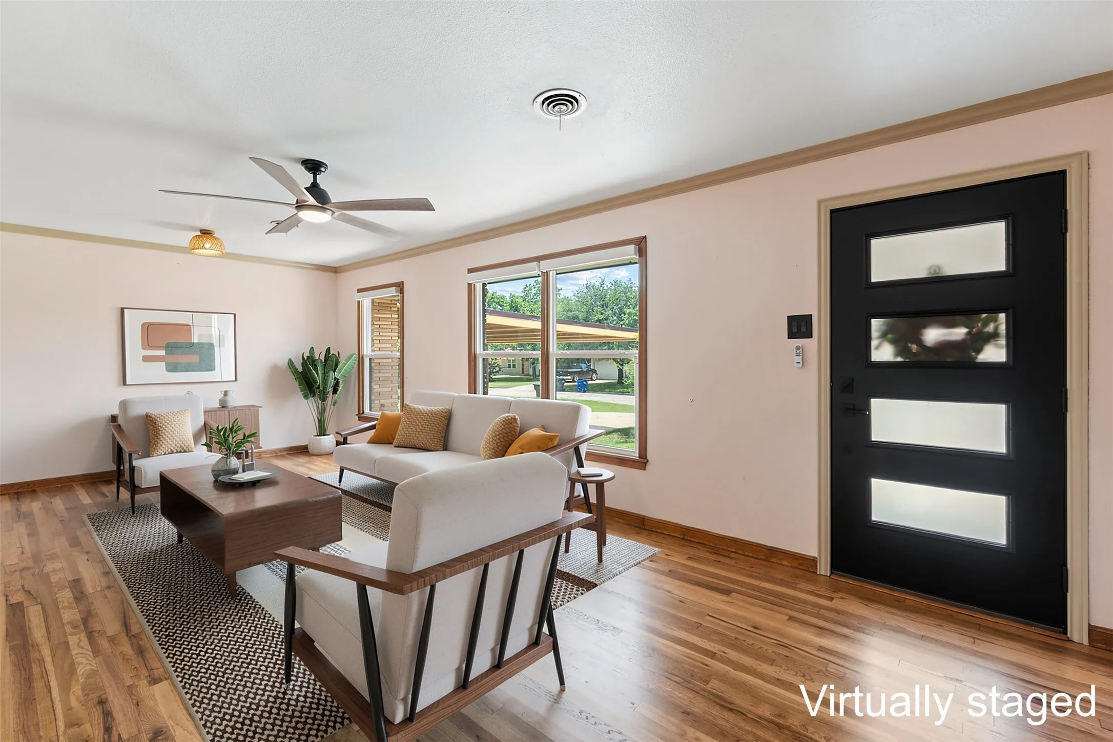 Spacious living area featuring wood-finish flooring, multiple windows providing ample light, a contemporary ceiling fan, and a modern entry door with frosted glass inserts