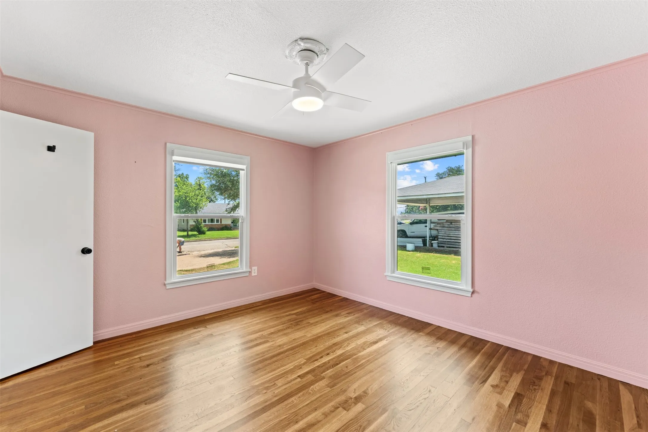 Bedroom featuring wood-finish flooring, two large windows, and a ceiling fan with integrated lighting