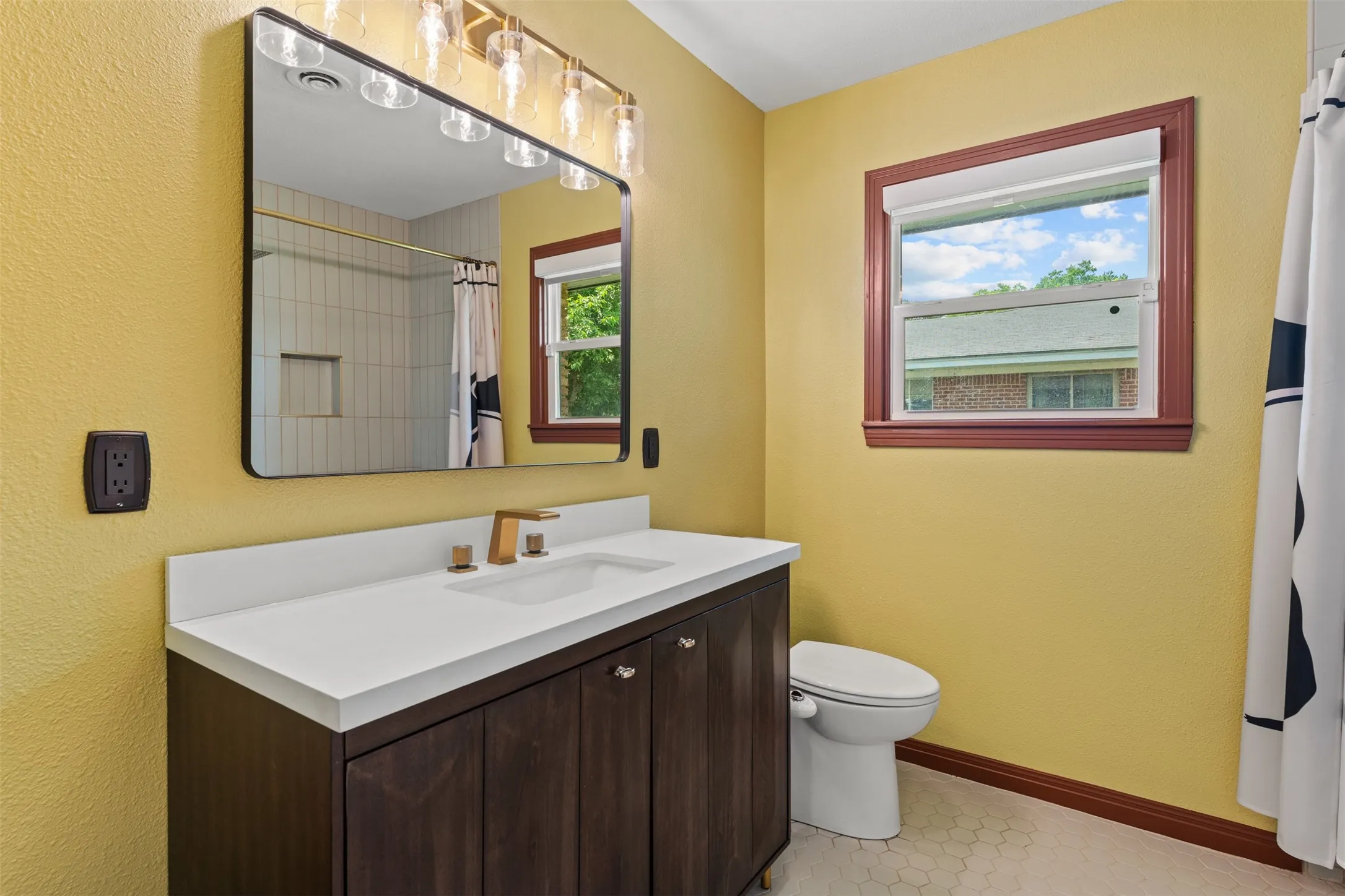 Bathroom featuring a dark wood-finish vanity with a white solid surface countertop, an undermount sink, and a gold-tone faucet