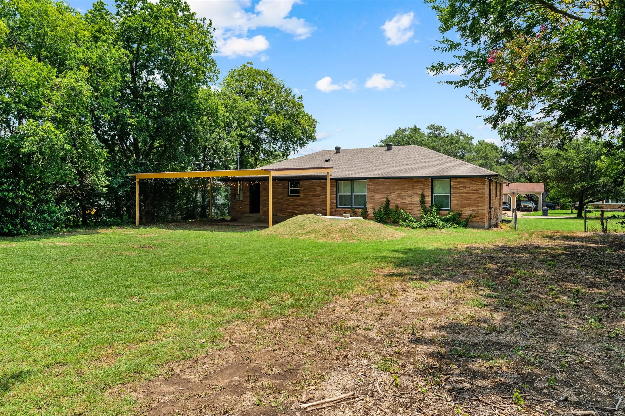 Expansive backyard featuring a partial grass lawn, mature trees, and a covered patio area