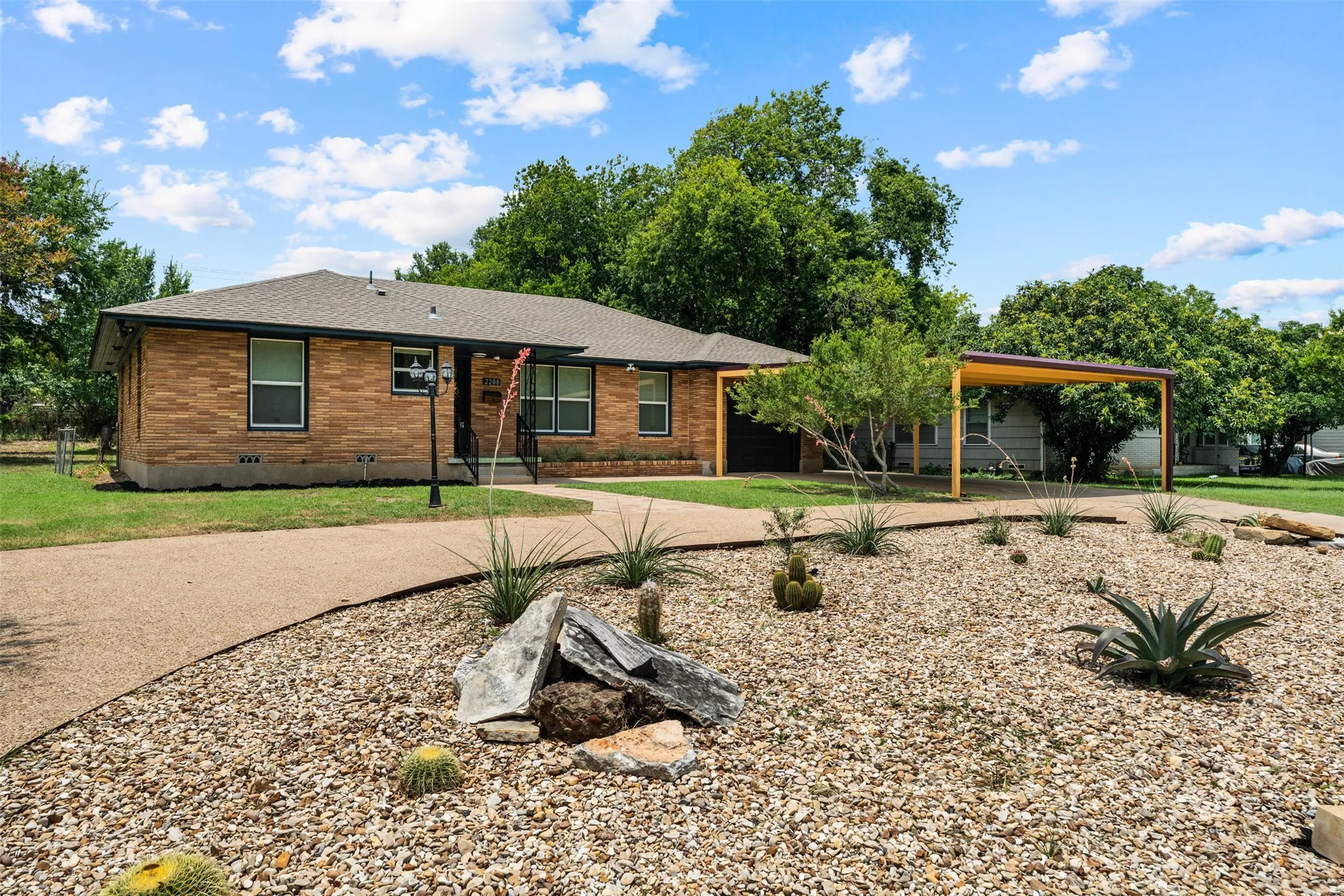 Brick exterior featuring a covered entry, dark-framed windows, and a detached carport