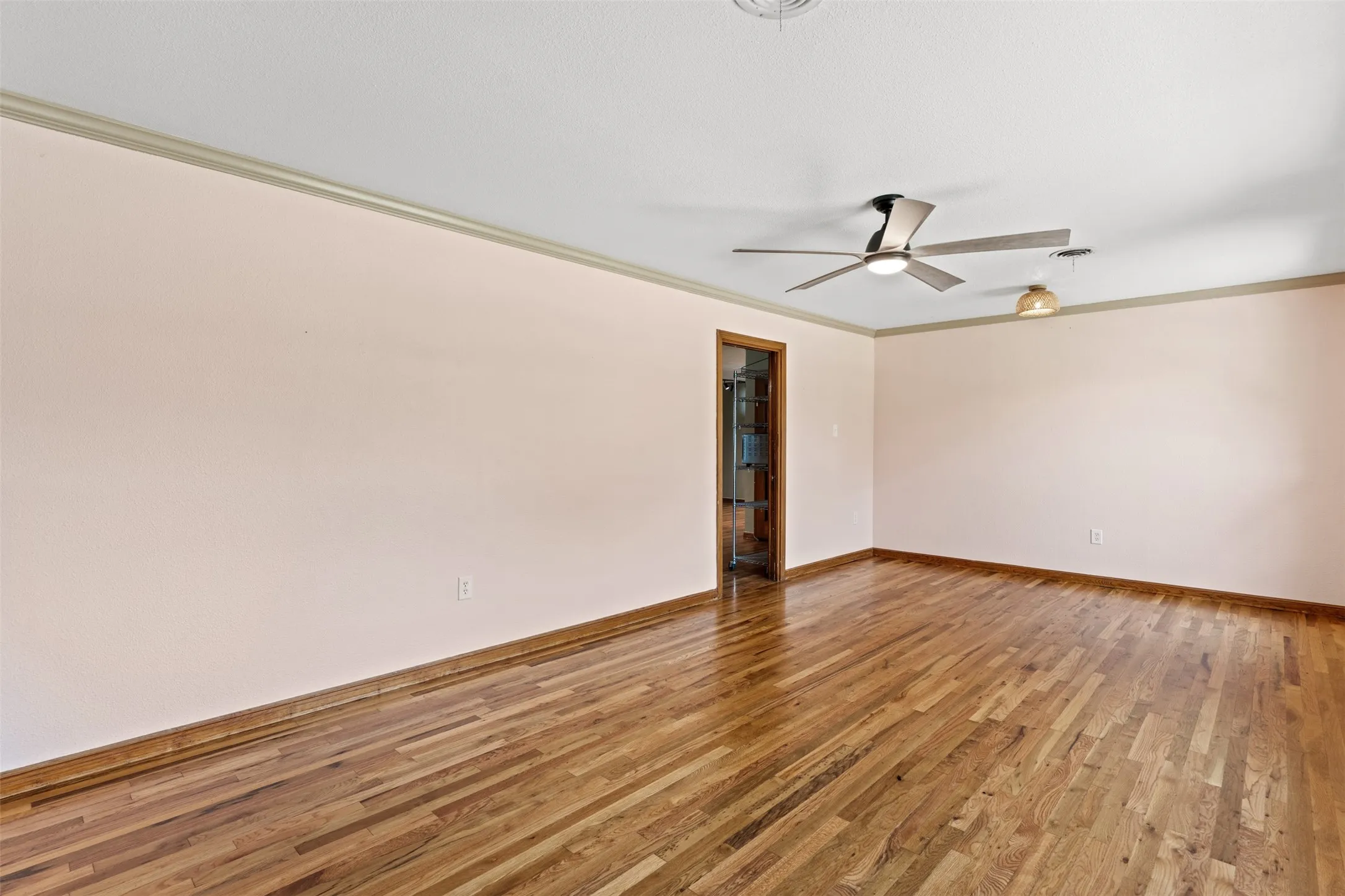 Spacious interior room featuring wood-finish flooring, light-toned walls, and crown molding