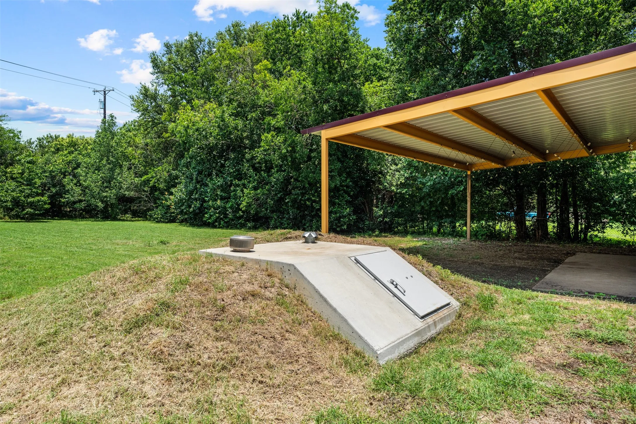 Concrete storm shelter with an accessible entrance, situated on a grassy mound