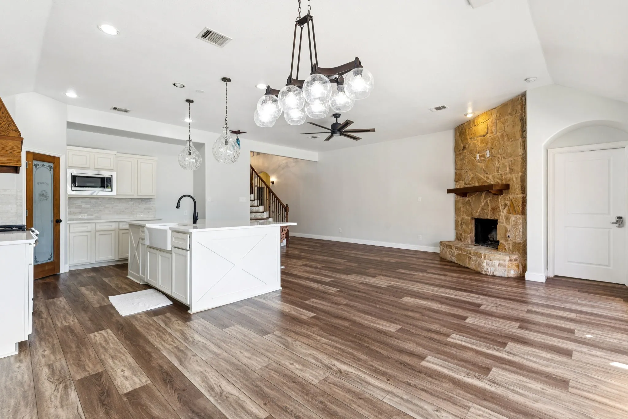 Kitchen featuring decorative light fixtures, backsplash, a fireplace, dark wood-style floors, and an island with sink