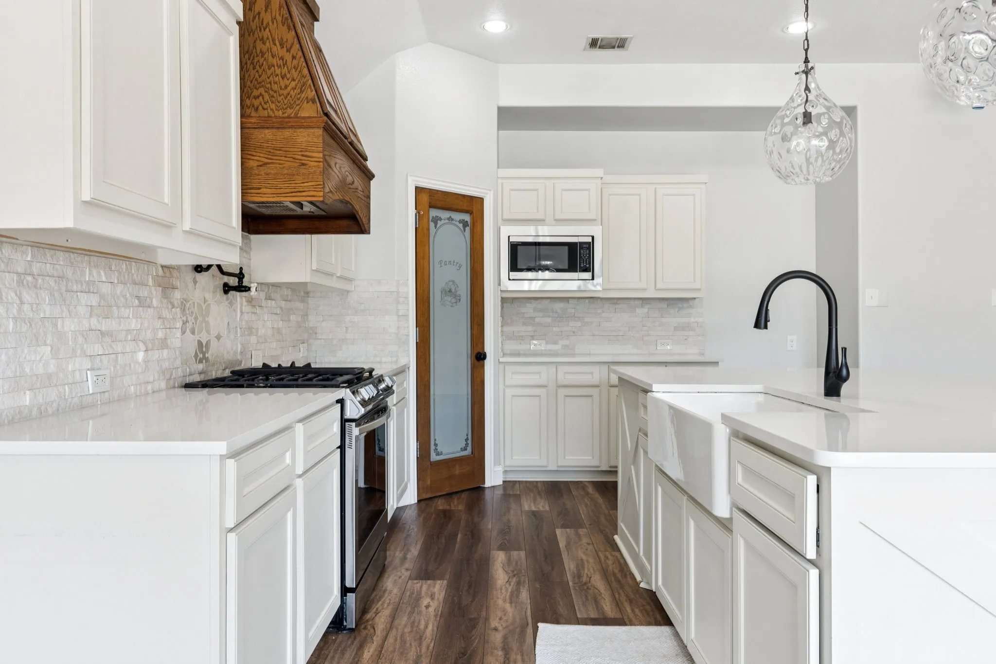 Kitchen featuring appliances with stainless steel finishes, decorative light fixtures, dark wood-style flooring, premium range hood, and light stone counters