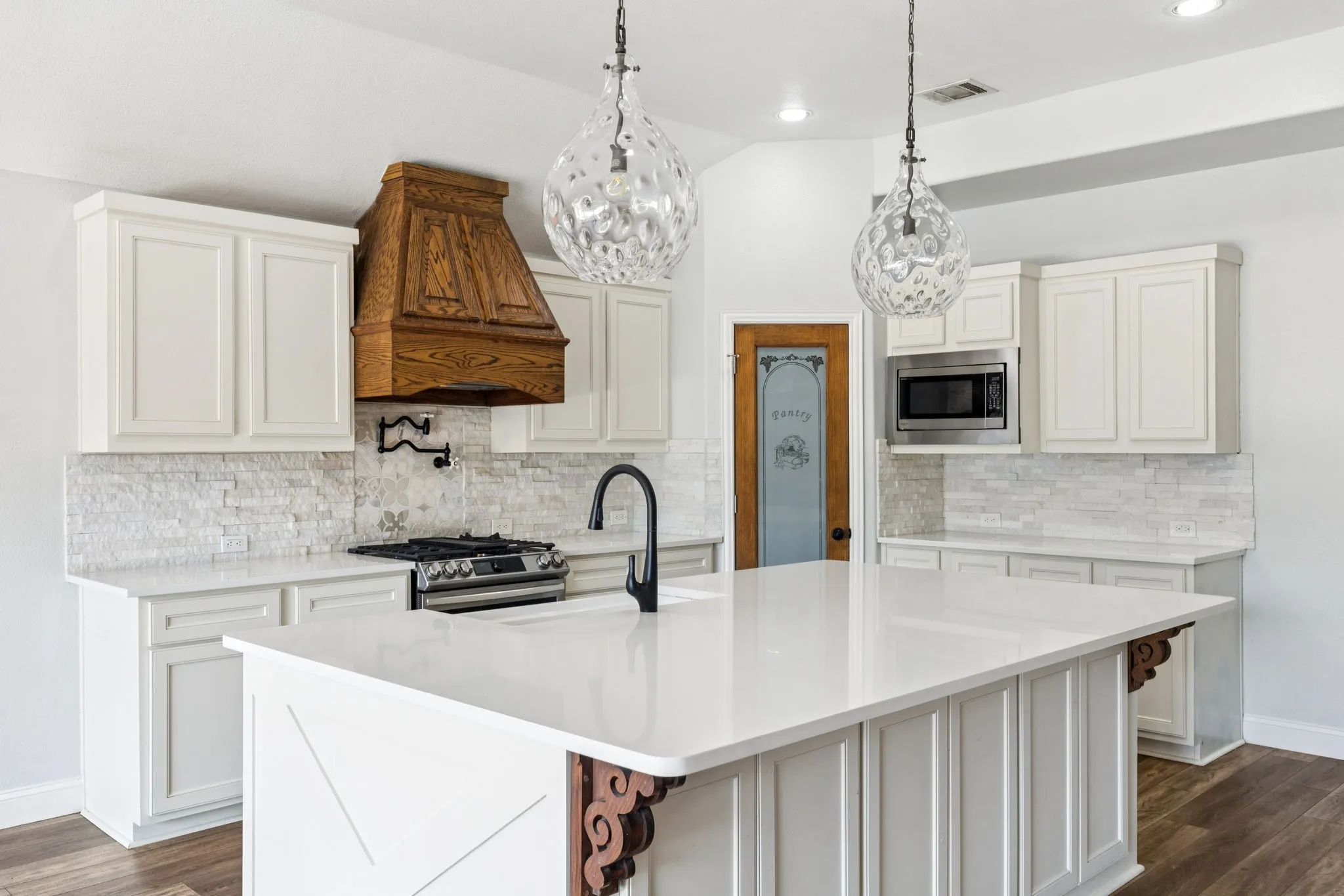 Kitchen with dark wood-type flooring, backsplash, decorative light fixtures, a center island with sink, and recessed lighting