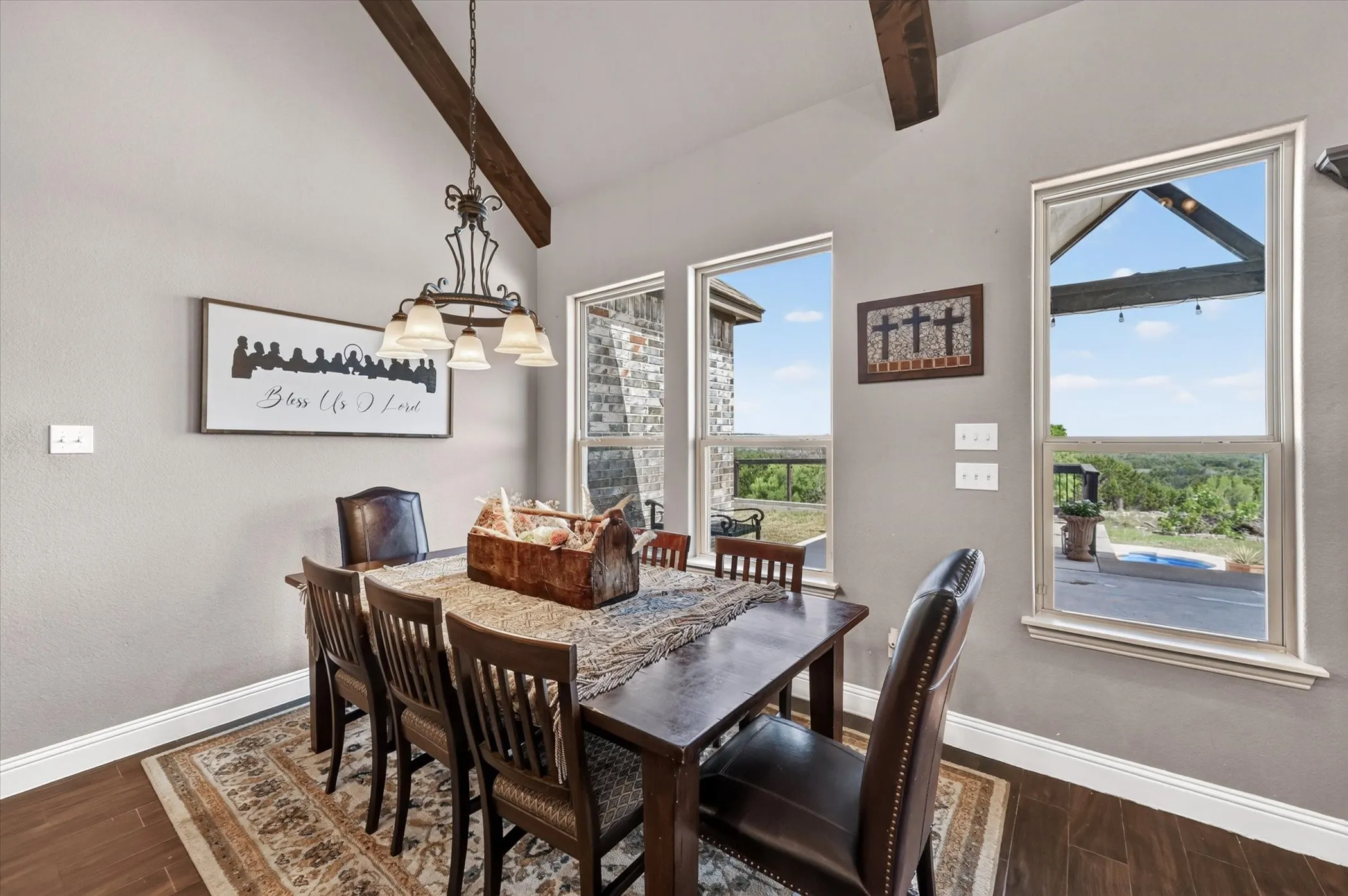 Dining area featuring wood-finish flooring, vaulted ceilings with exposed beams, an ornate chandelier, and multiple windows