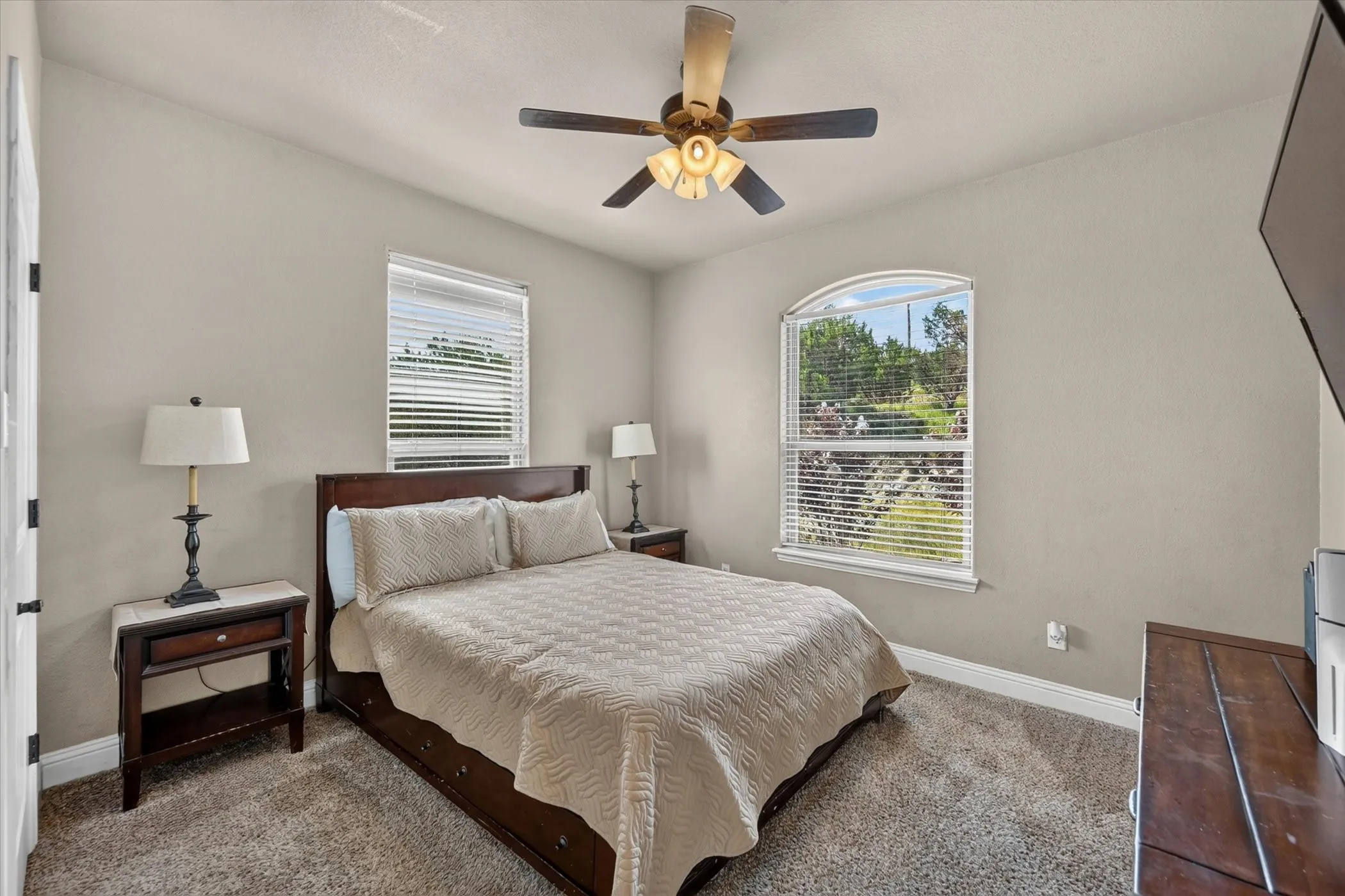 Carpeted room featuring a ceiling fan with integrated lighting, a rectangular window with blinds, and an arched window with blinds
