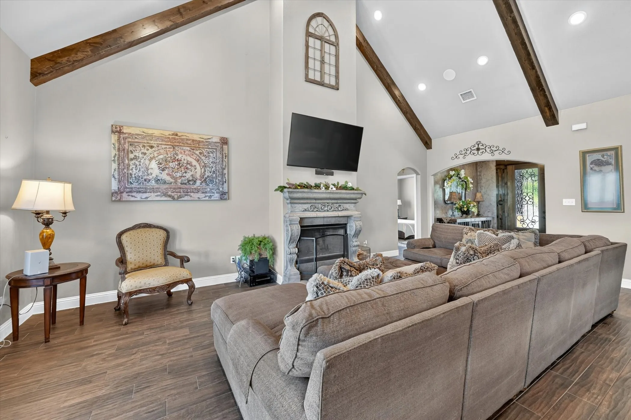 Spacious living area featuring vaulted ceilings with exposed wood beams, a stone-finish fireplace, and wood-finish flooring