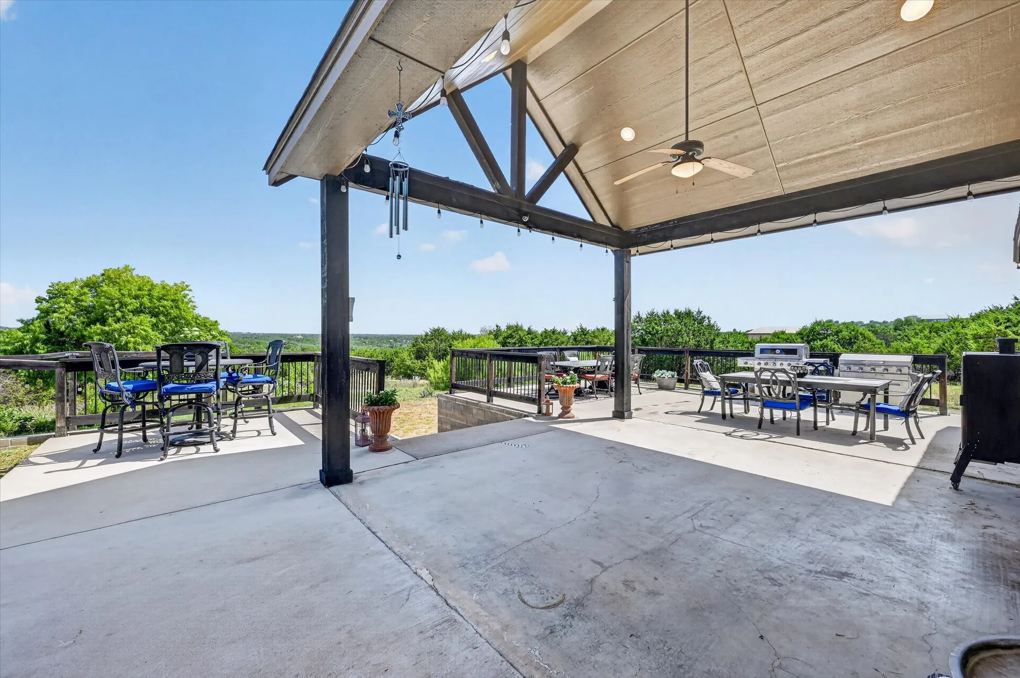 Expansive covered outdoor living area featuring a concrete patio, exposed beam ceiling with a ceiling fan, and string lighting