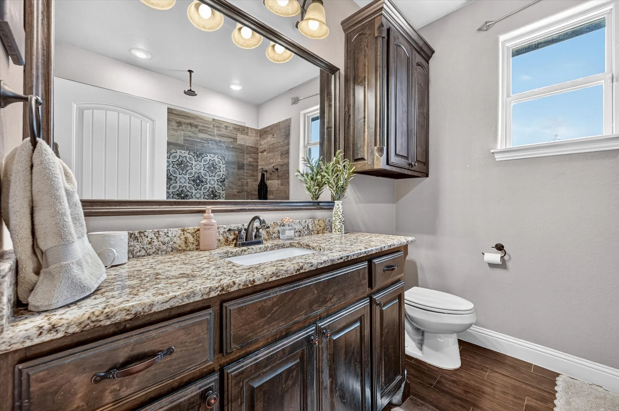 Bathroom featuring a dark wood-finish vanity with a light-toned patterned countertop, an undermount sink, and a framed mirror with overhead lighting