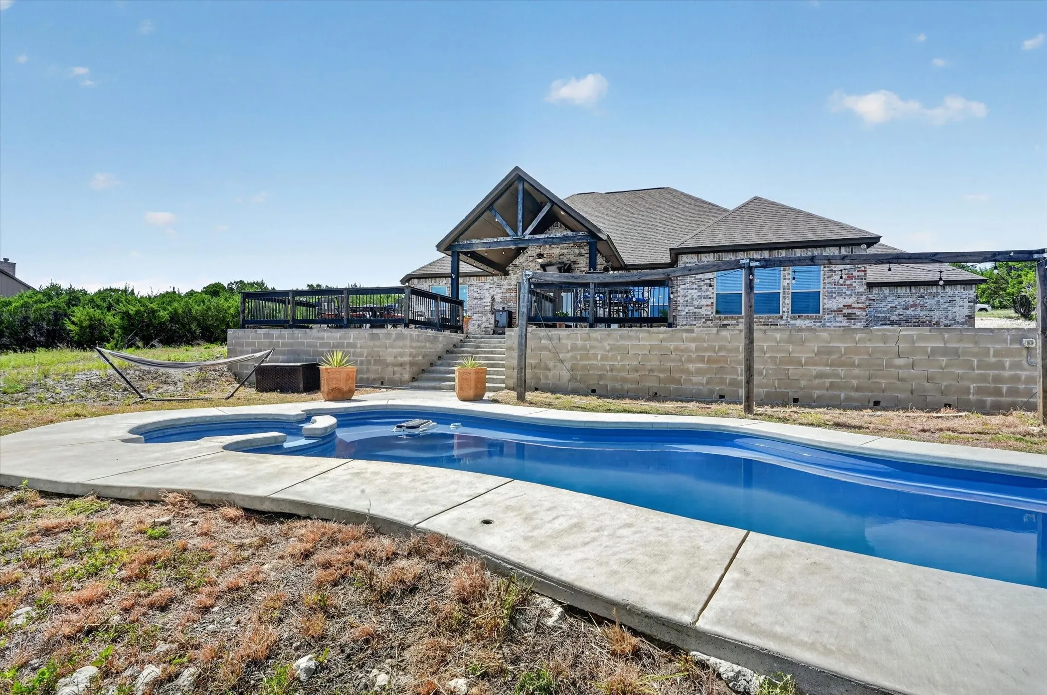 In-ground swimming pool with integrated spa, concrete decking, and steps leading to a raised stone and brick exterior