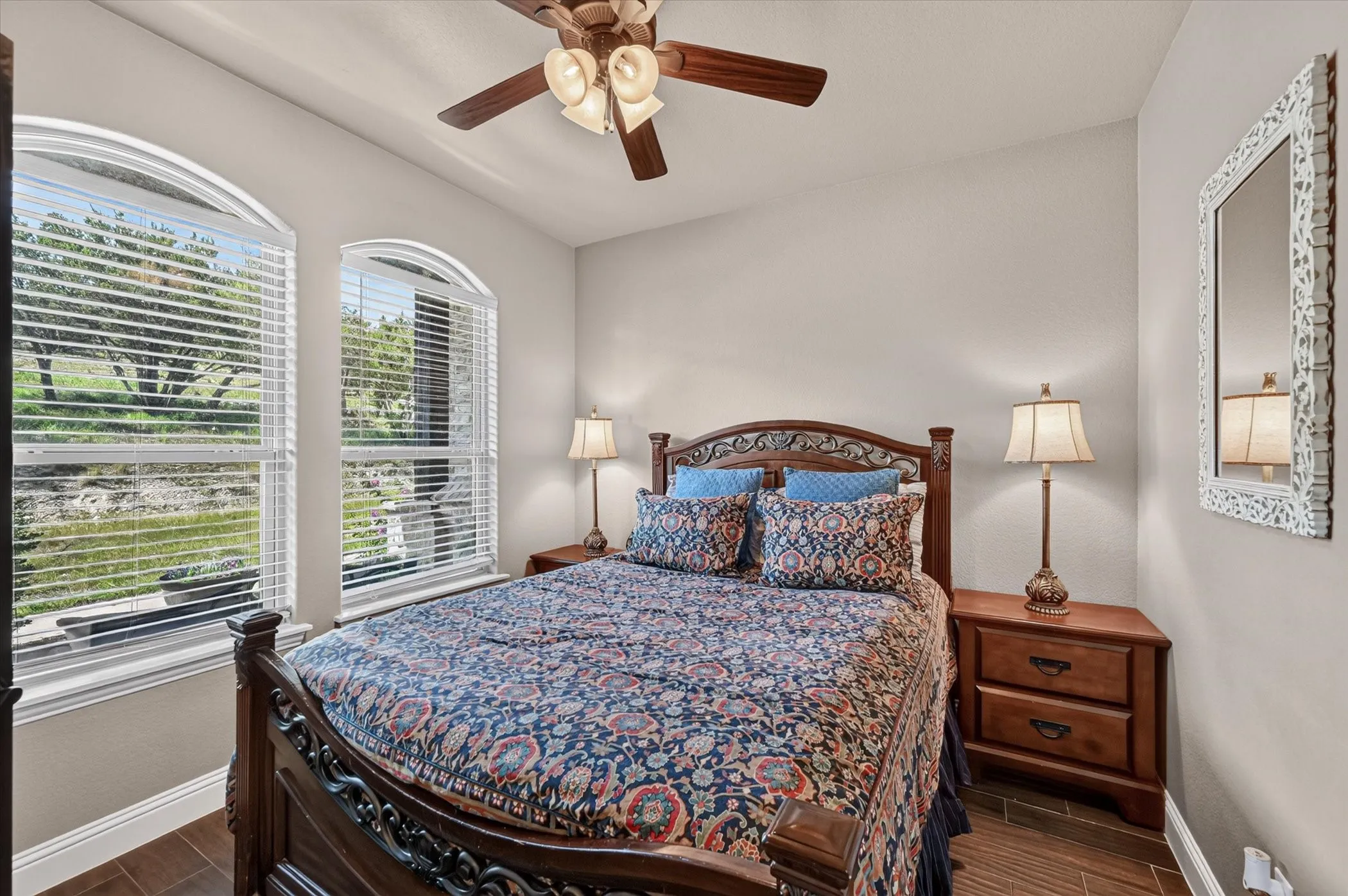 Room featuring two arched windows with blinds, wood-finish flooring, and a ceiling fan with integrated lighting. Currently set up as a guest bedroom as it does have a closet. Easily could be used as a home office or study.