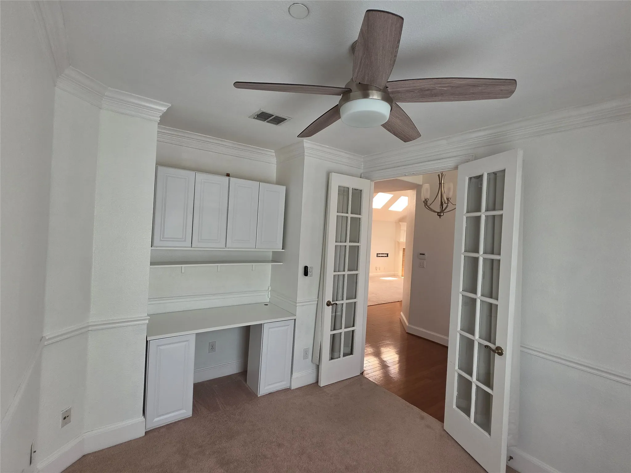 Room featuring crown molding, an integrated desk with upper and lower cabinetry, ceiling fan with light fixture, and French doors