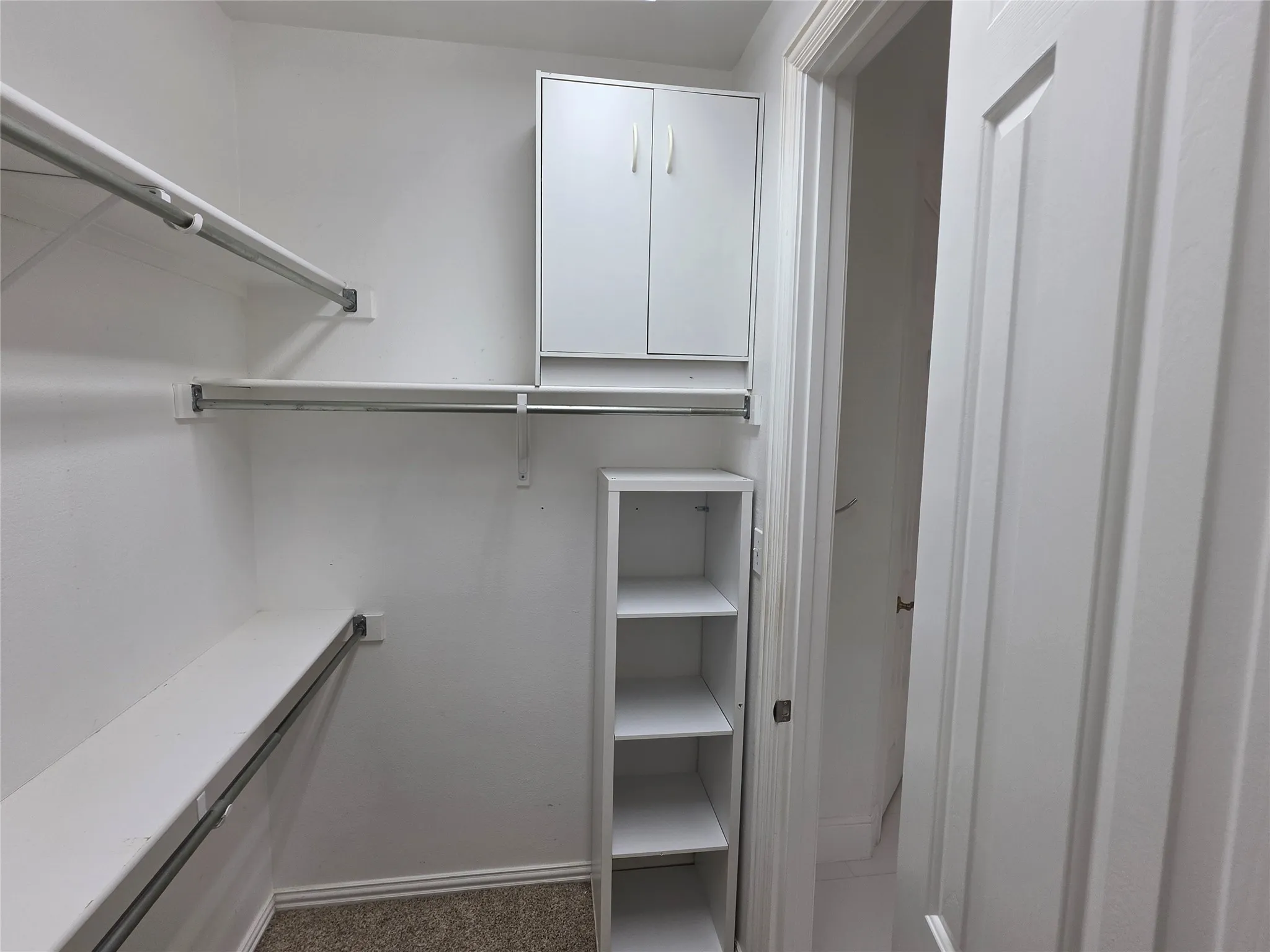 Walk-in closet featuring white built-in shelving, two hanging rods, and a white cabinet with double doors