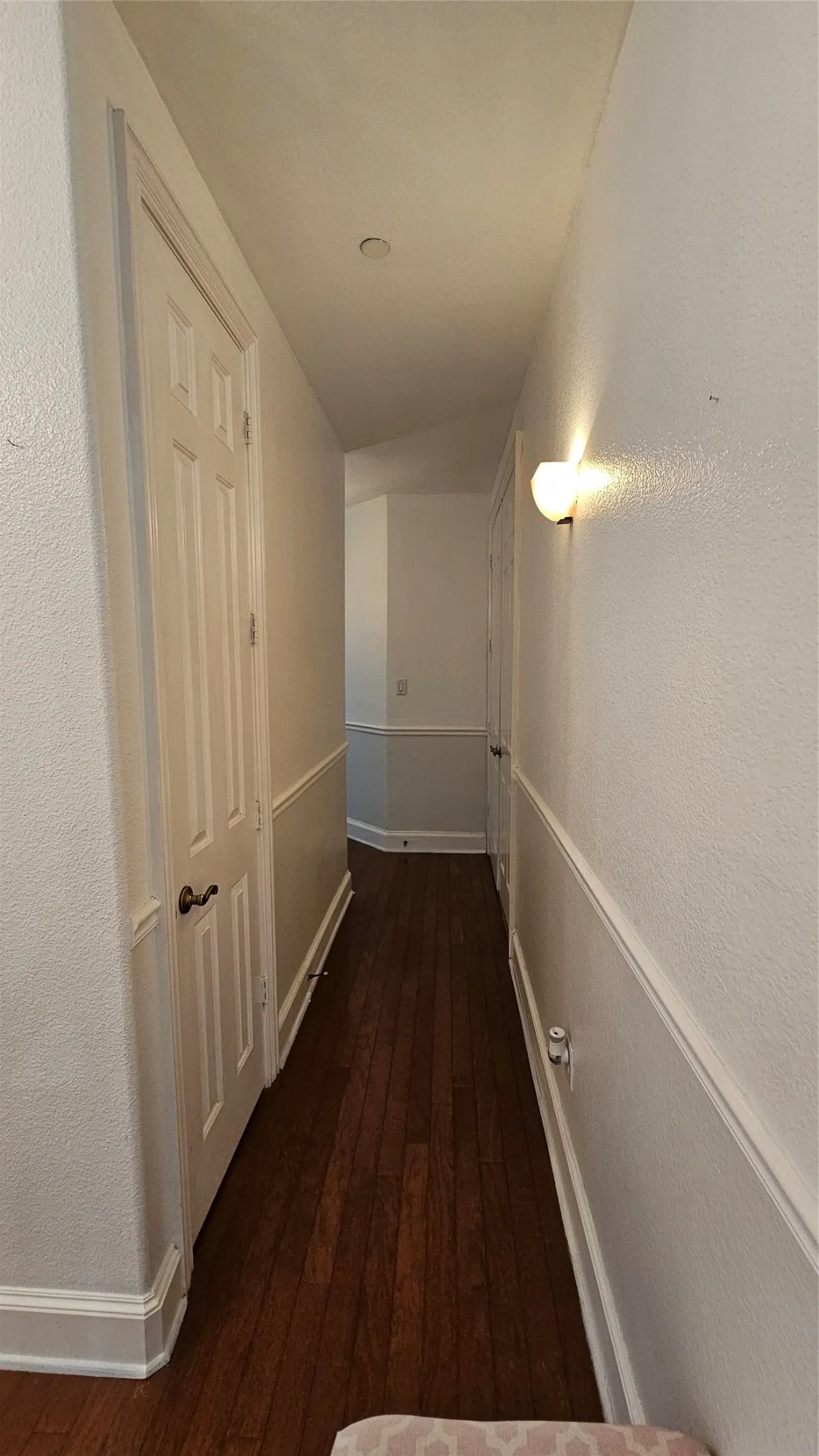 Hallway featuring wood-finish flooring, white paneled doors, wainscoting, wall sconce lighting, and recessed ceiling lighting