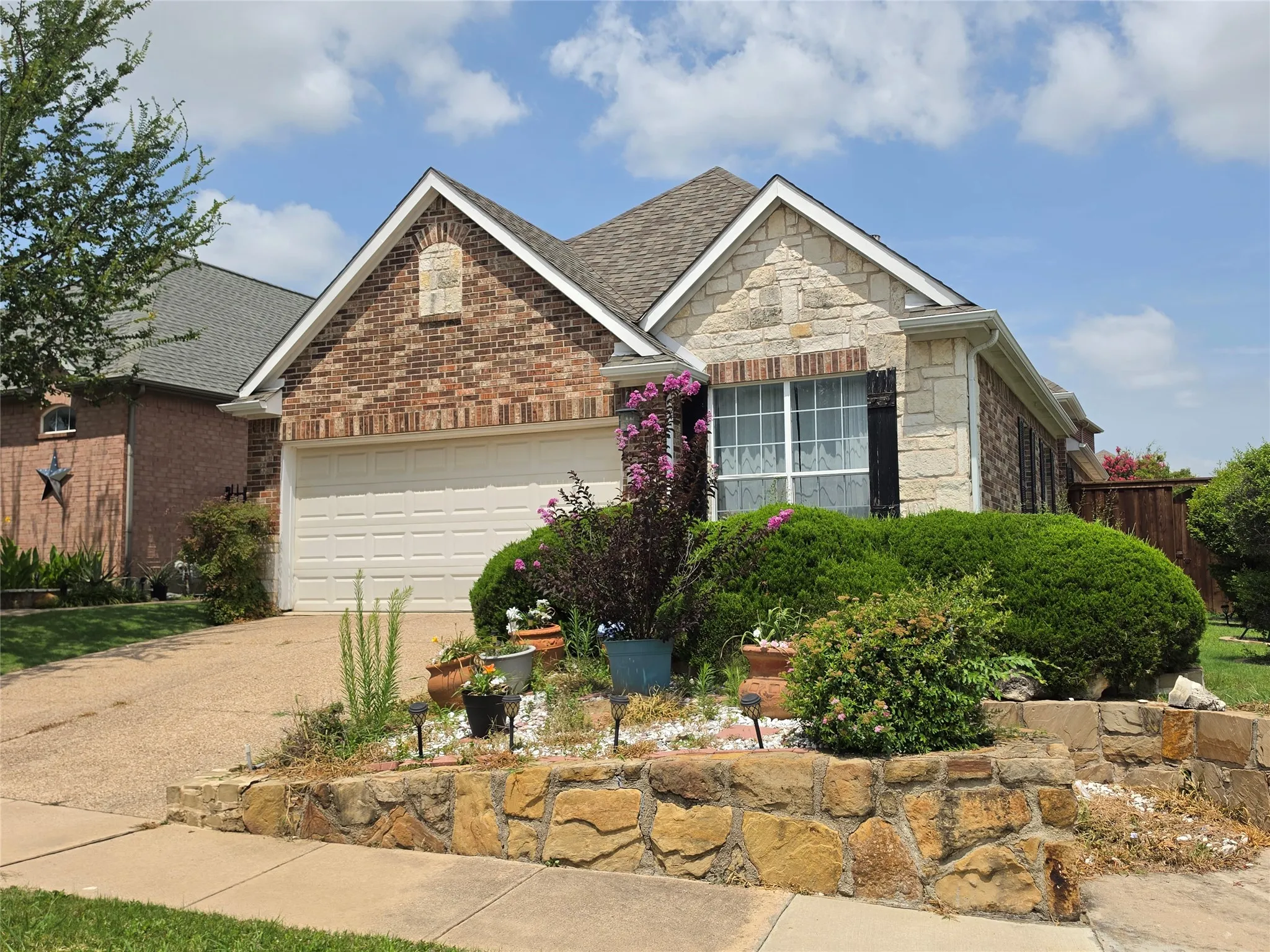 Front exterior featuring a brick and stone facade, an attached garage, and a tiered stone retaining wall