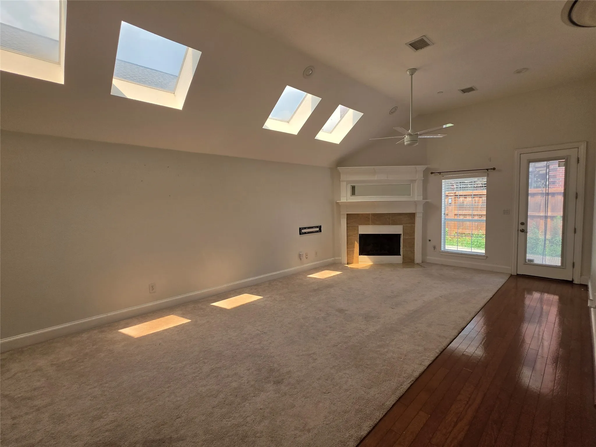 Spacious interior featuring a vaulted ceiling with multiple skylights, a fireplace with a mantel, a ceiling fan, and mixed flooring with carpet and wood-finish