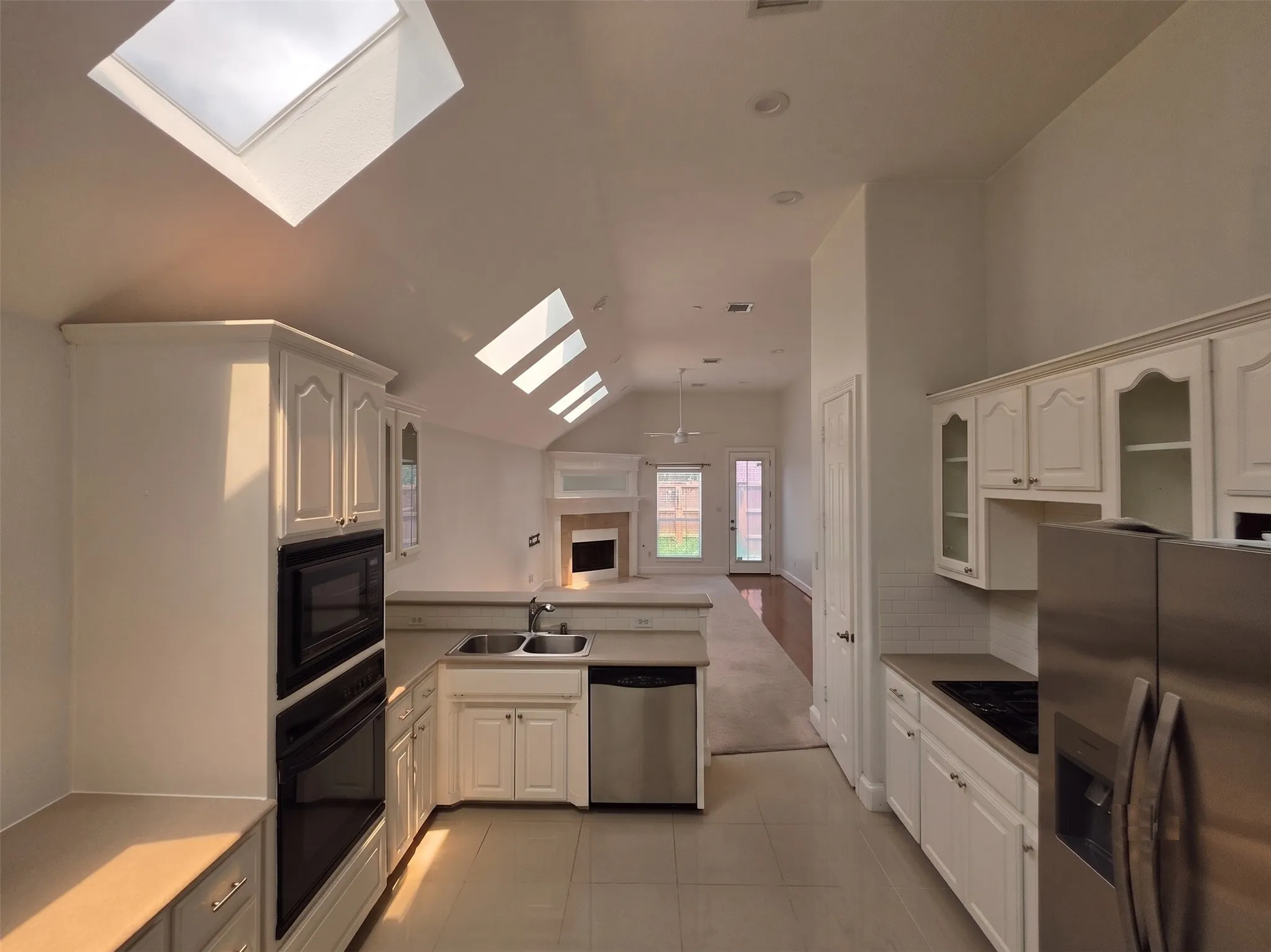 Kitchen featuring white cabinetry with glass inserts, dual stainless steel sink, integrated stainless steel appliances, and tile flooring