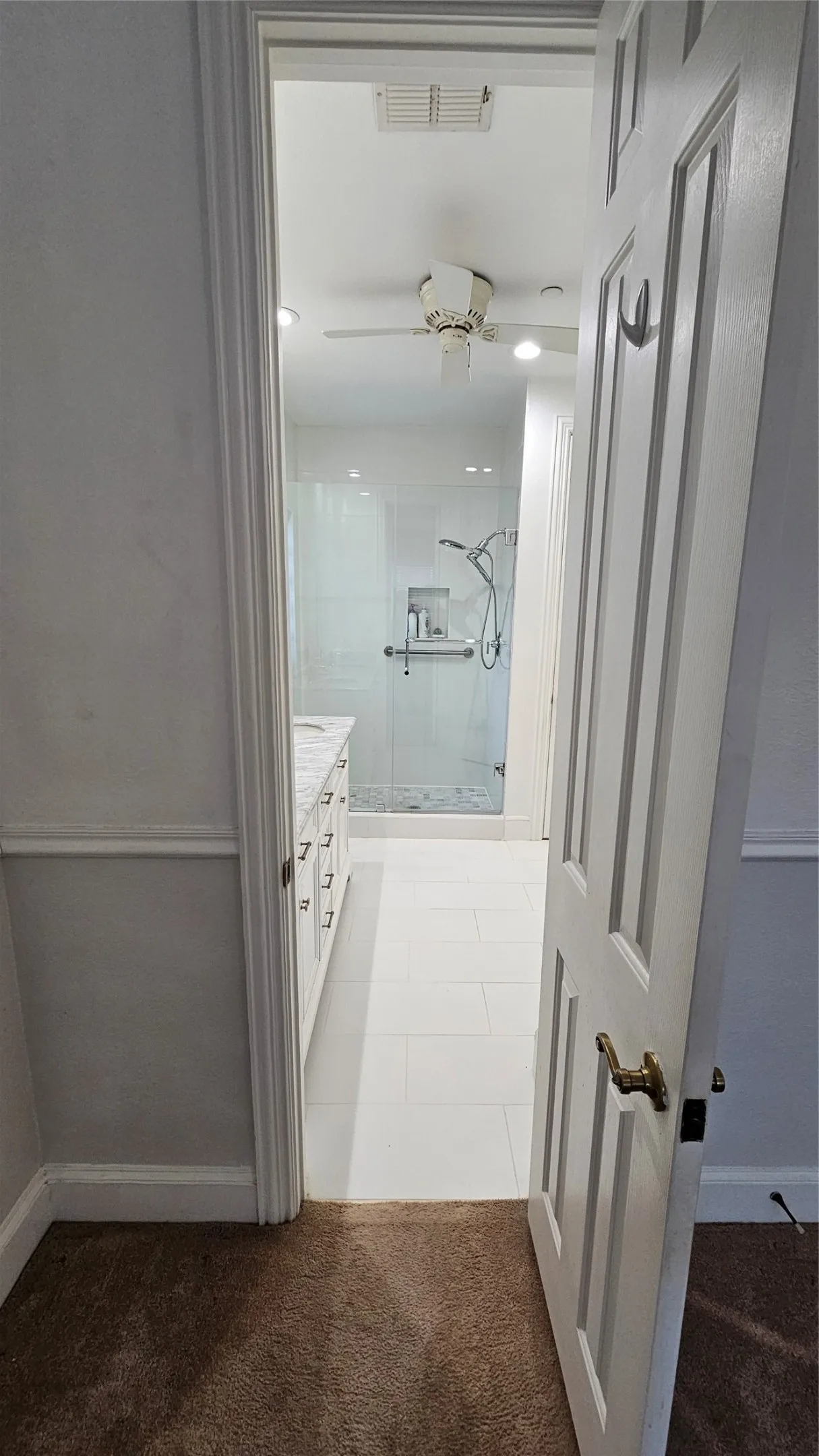 Bathroom featuring a white tiled floor, a glass-enclosed shower, and a vanity with a light-colored countertop