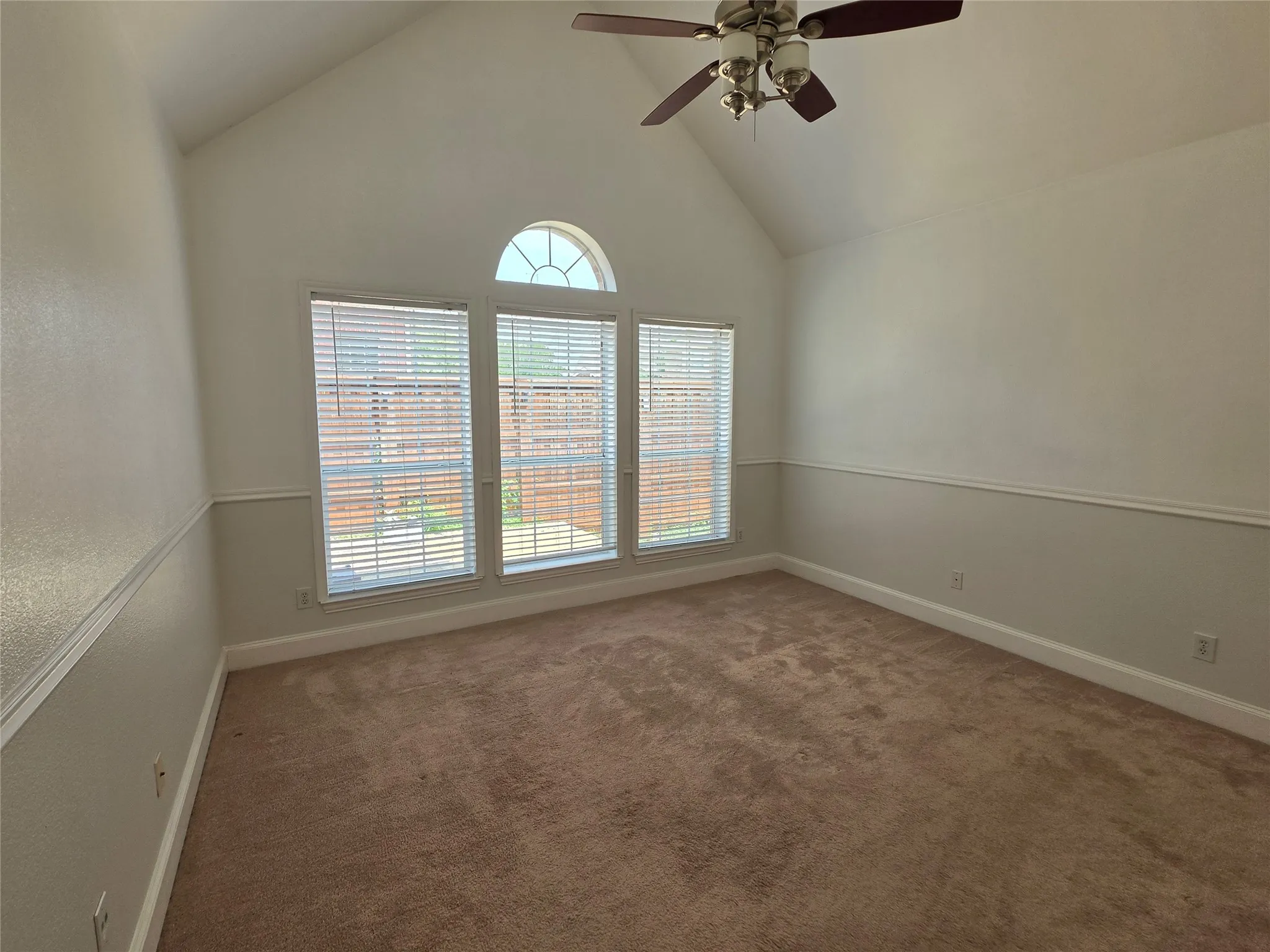Vaulted ceiling room featuring three large windows with blinds and an arched transom window