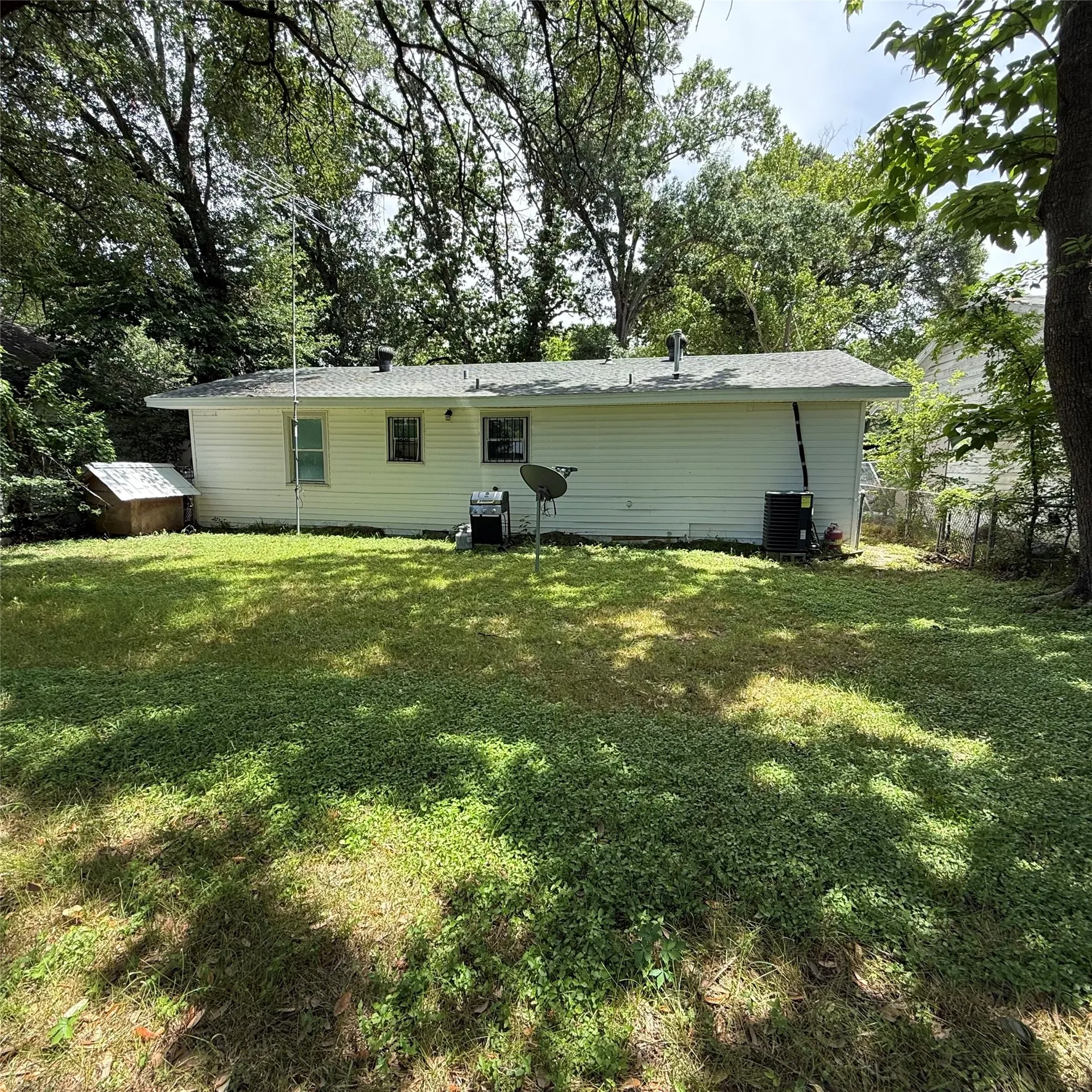 Expansive rear yard featuring a white siding exterior, shingle roofing, and mature perimeter trees