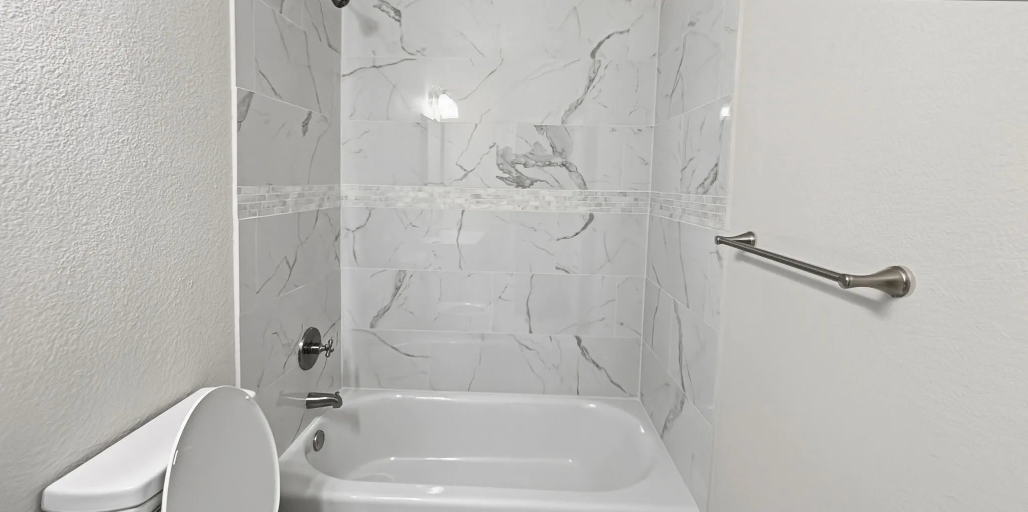 Bathroom featuring a white bathtub, white marble-patterned wall tiles, decorative accent tile band, and brushed nickel fixtures