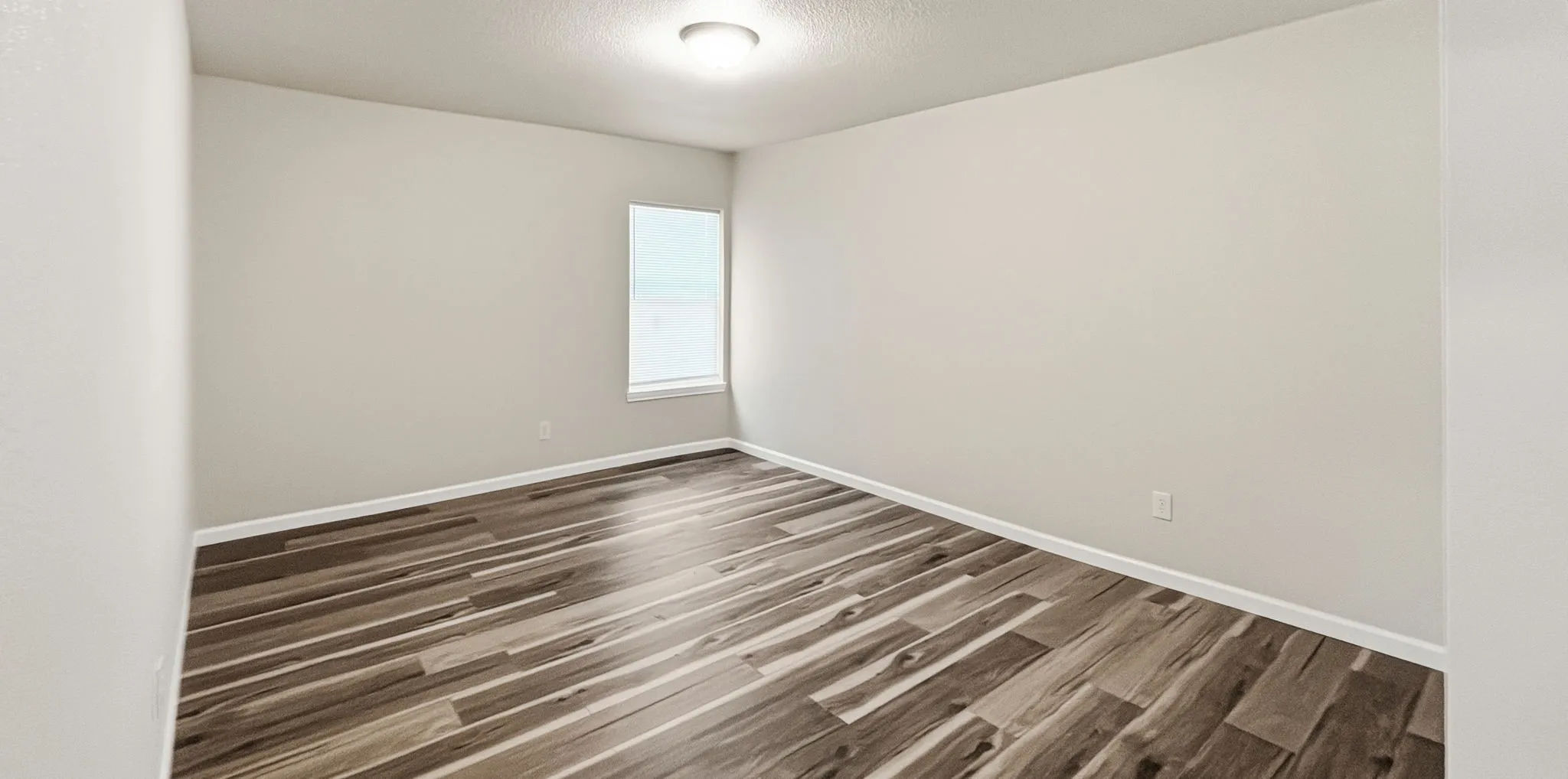 Room featuring wood-finish flooring, neutral wall tones, white baseboards, and a single window