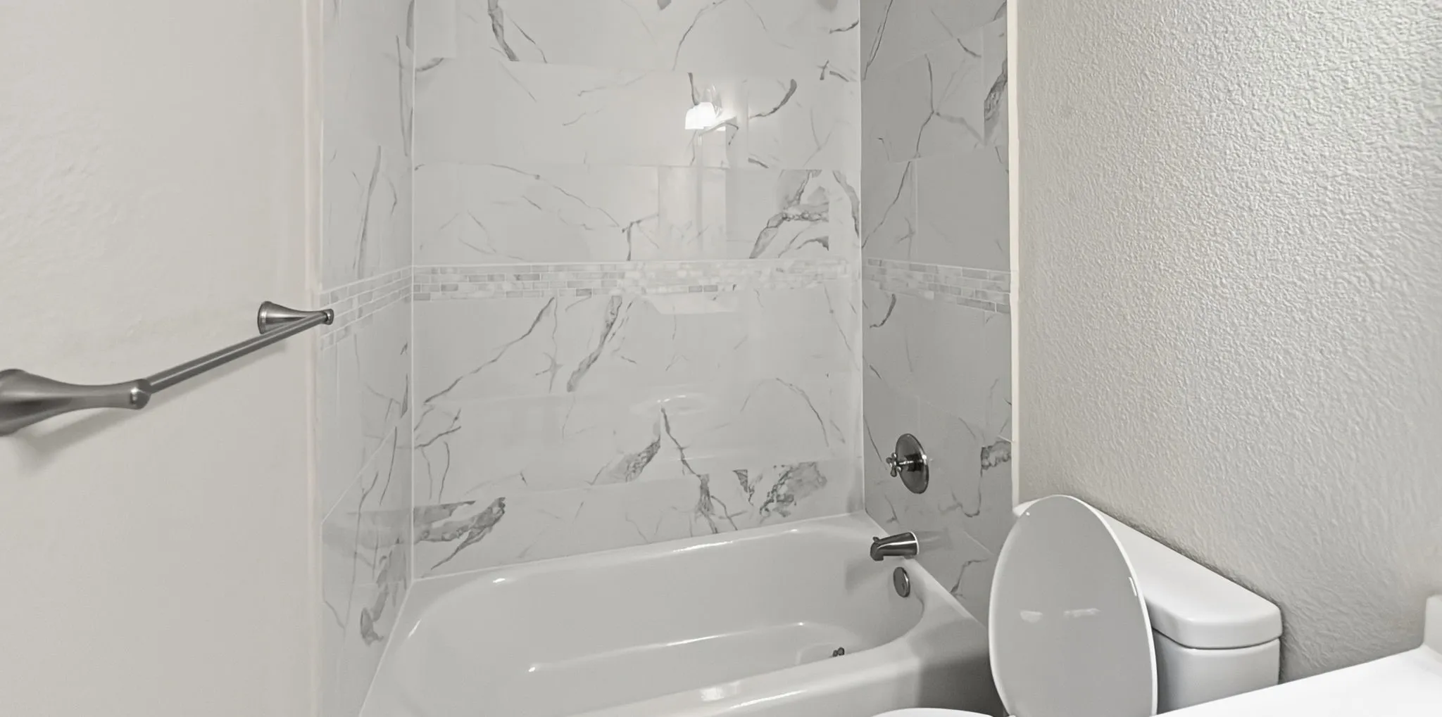 Full bathroom featuring a white bathtub, marble-patterned tile surround, decorative tile accent band, and a brushed nickel towel bar