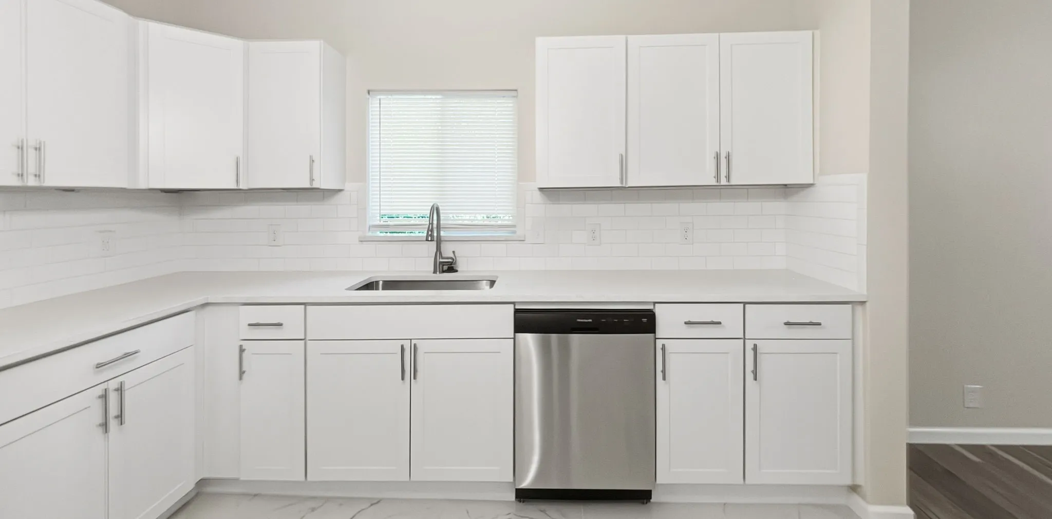 Kitchen featuring white shaker cabinetry, light-toned countertops, subway tile backsplash, stainless steel sink with a gooseneck faucet, and a stainless steel dishwasher