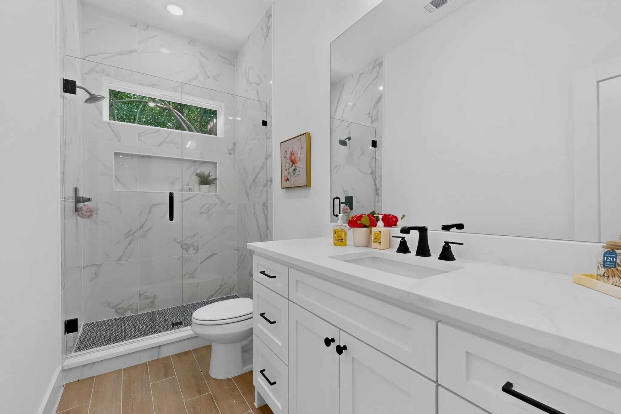 Modern bathroom featuring a frameless glass shower enclosure with marble-look tile surround and an inset product niche