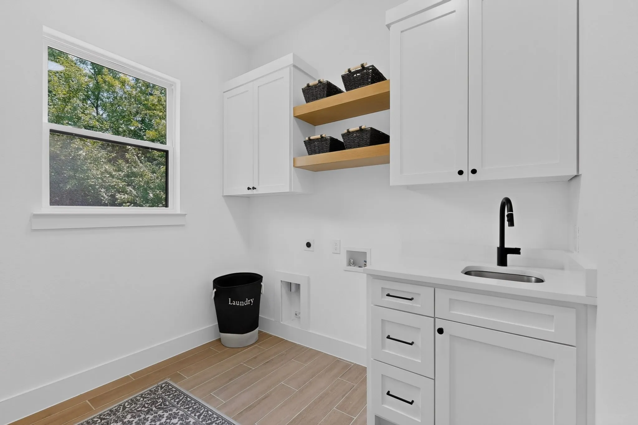 Bright utility room featuring white cabinetry, a built-in sink with a black faucet, light wood-finish flooring, and natural light from a double-hung window