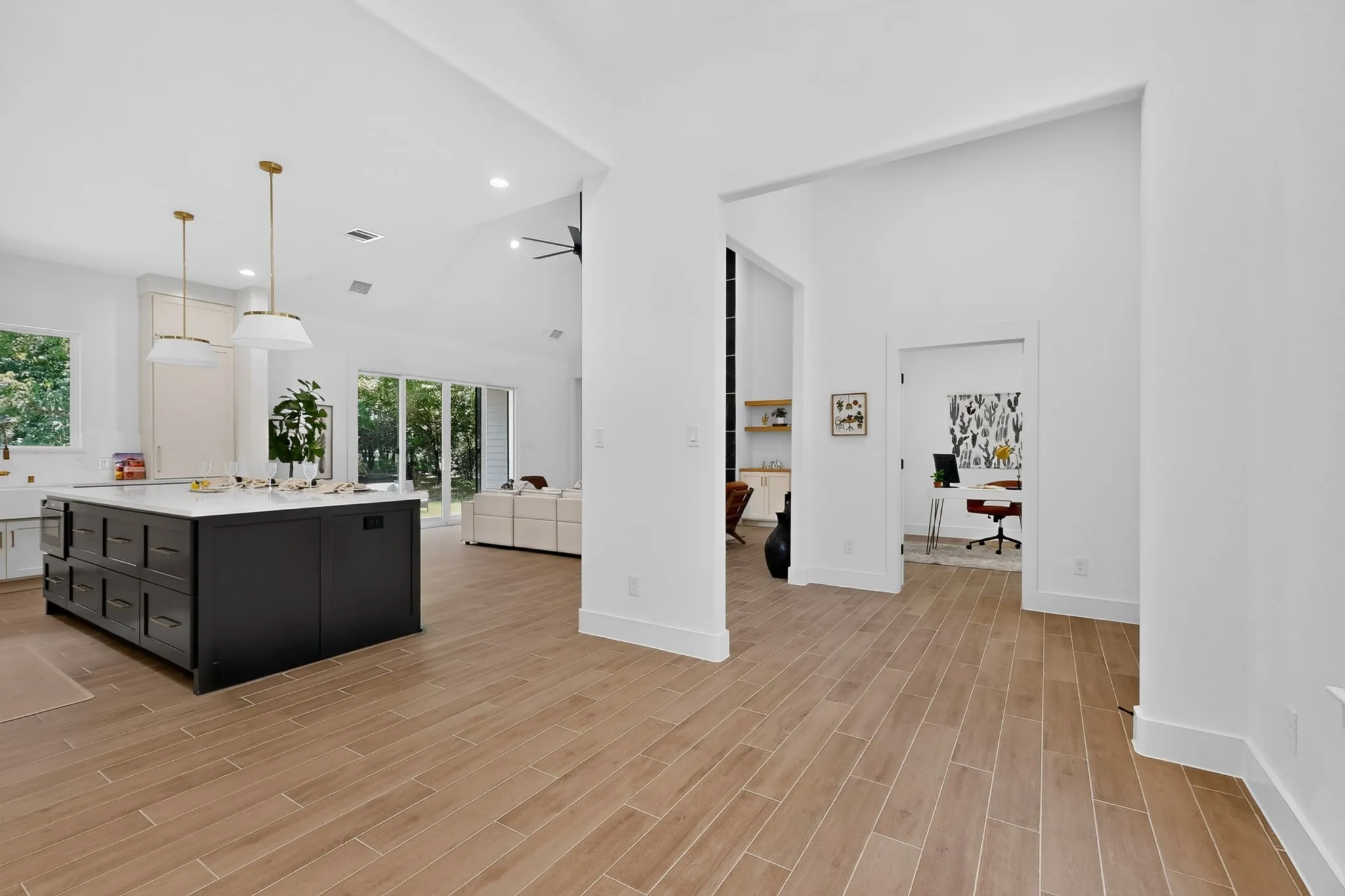 Open-concept living space with wood-finish flooring, a large kitchen island with ample storage, recessed lighting, and expansive sliding glass doors