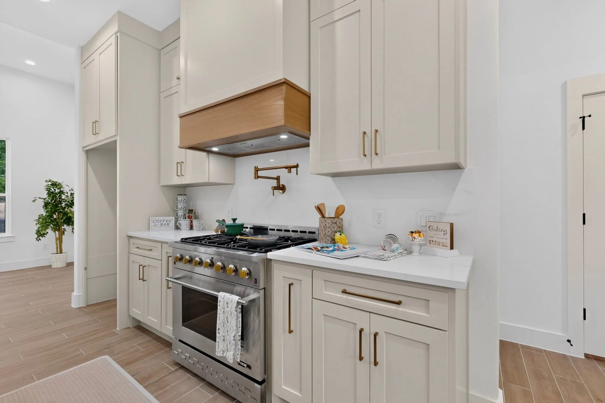 Gourmet kitchen featuring a stainless steel range with a pot filler, custom range hood, white shaker cabinetry, white countertops, and wood-finish flooring