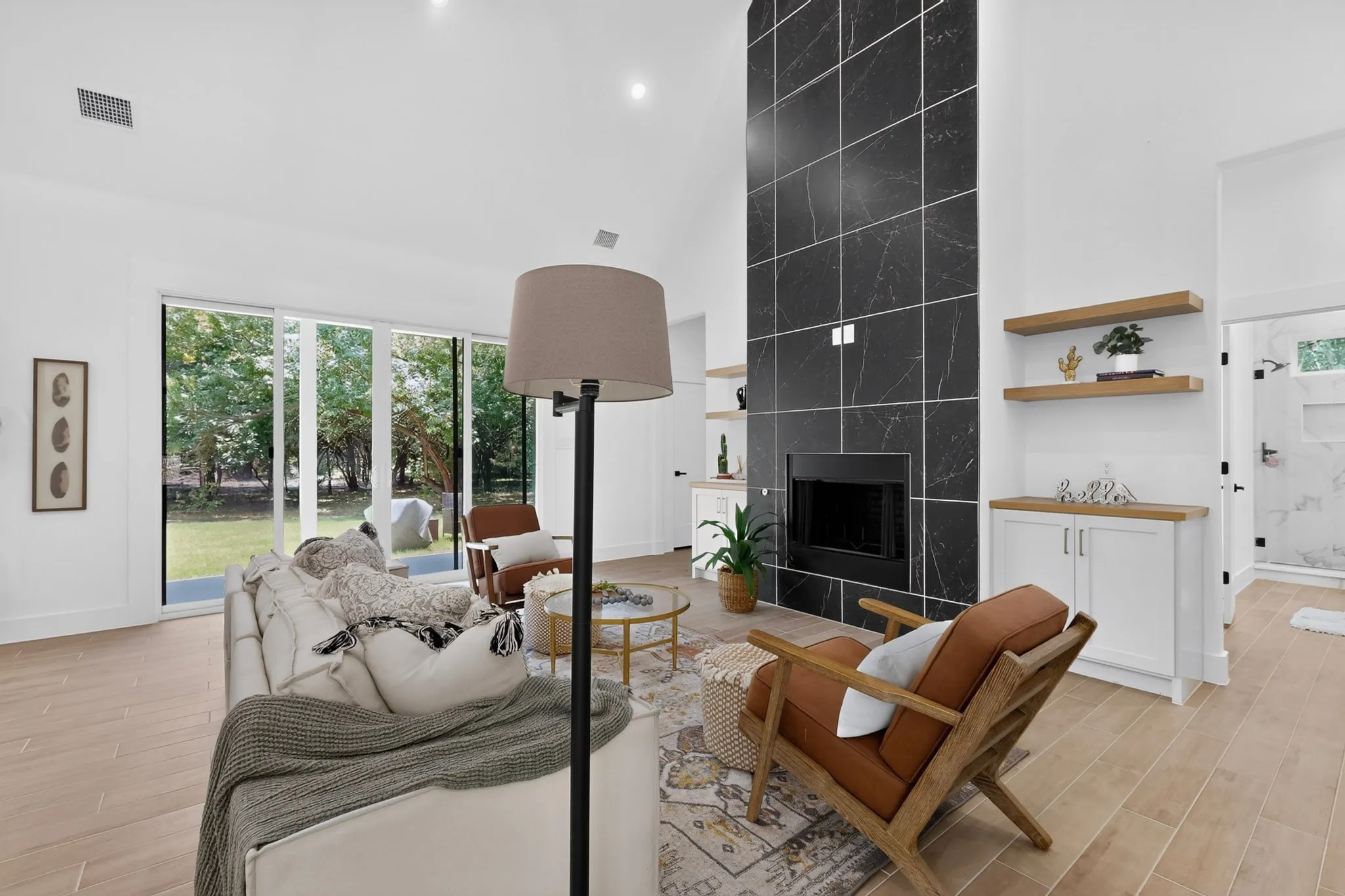 Vaulted ceiling living space featuring a floor-to-ceiling dark tile fireplace surround, light wood-finish flooring, and built-in shelving with lower cabinetry
