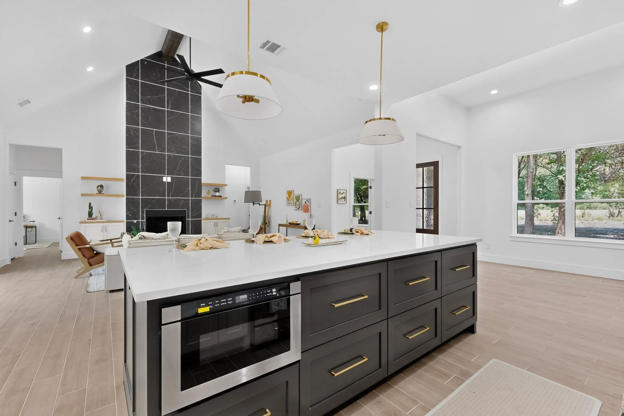 Large kitchen island featuring a white countertop, built-in microwave, and dark cabinetry with gold-toned hardware