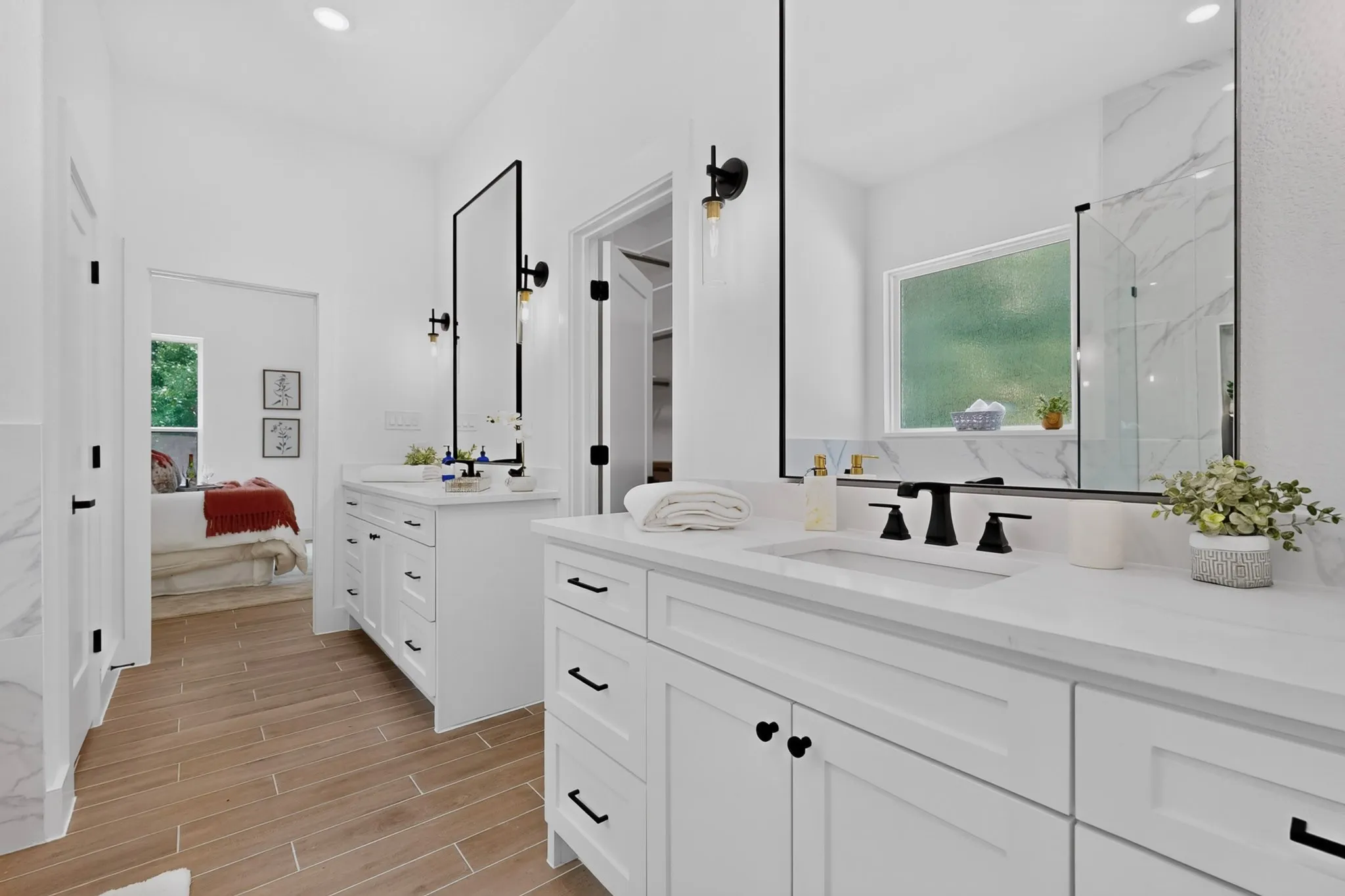 Bathroom featuring dual white vanities with integrated sinks, matte black fixtures, wood-finish flooring, and a walk-in shower with stone-look tile