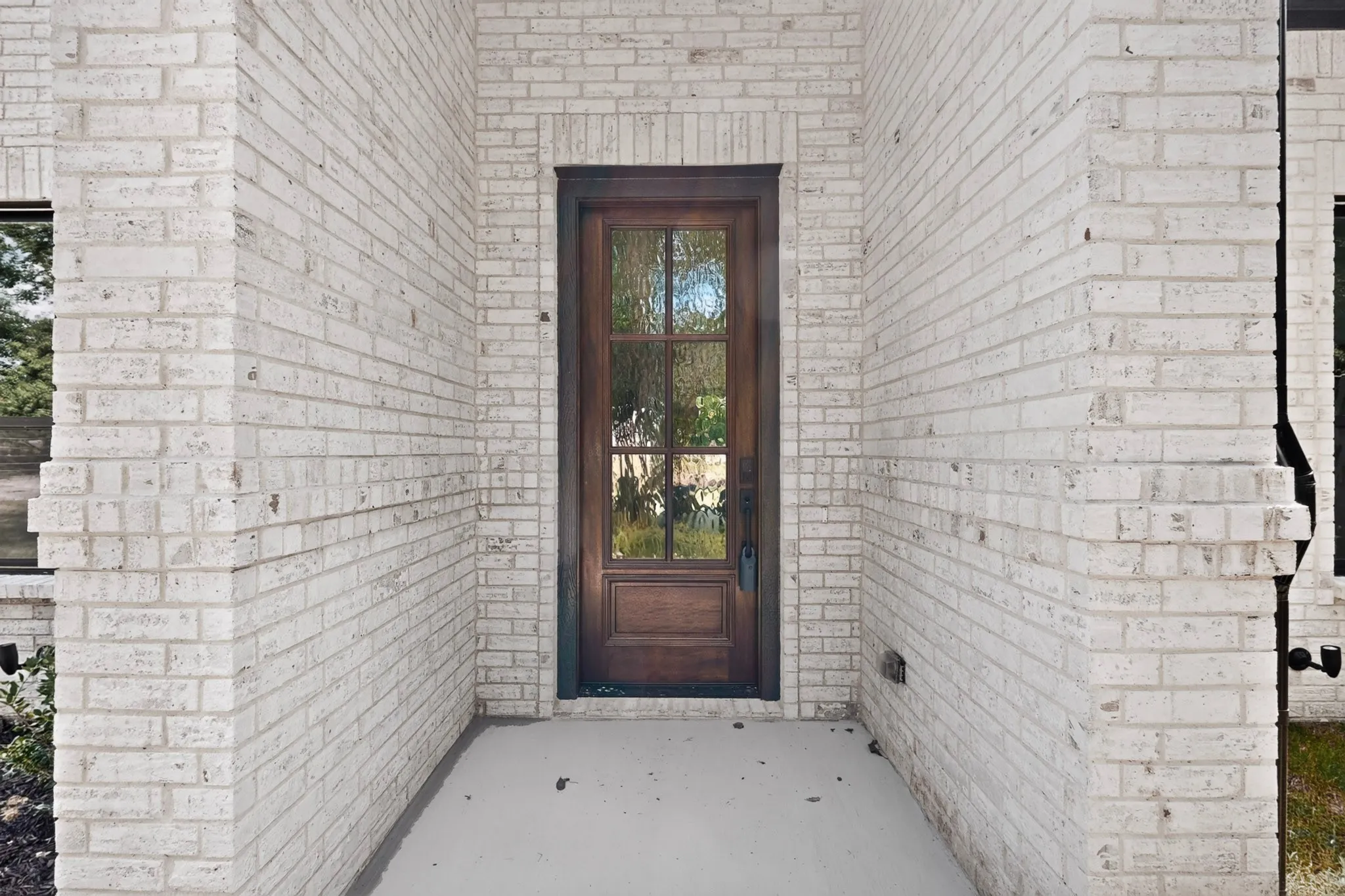 White brick exterior with a dark wood-finish front door, featuring multiple glass panes and a dark frame