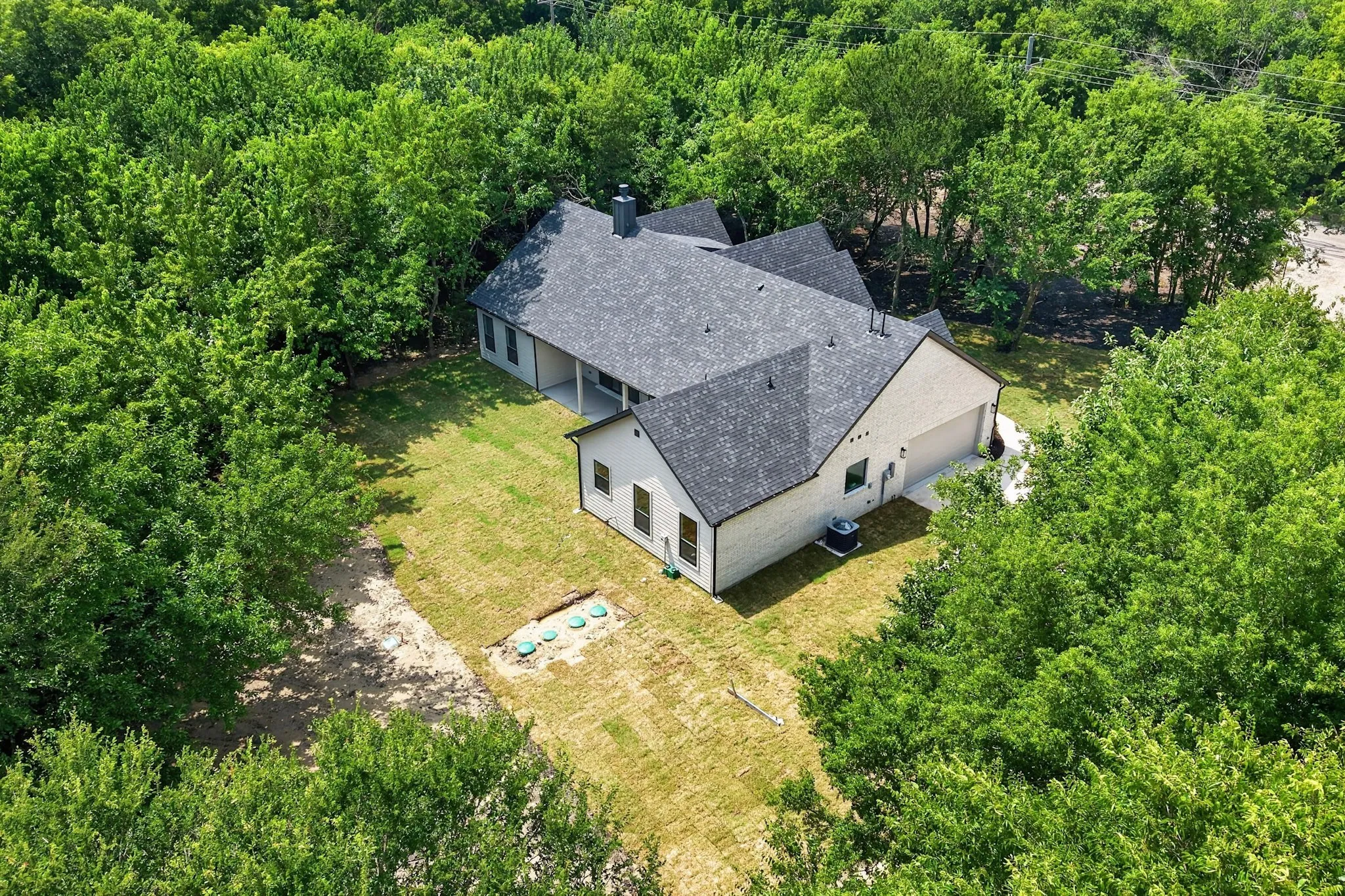 Modern residence featuring a dark shingle roof, light-colored exterior siding, an attached two-car garage, and a covered back patio
