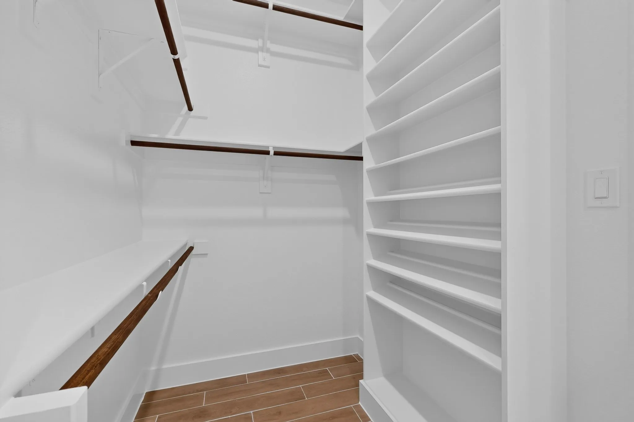 Spacious walk-in closet featuring white built-in shelving, multiple hanging rods, and wood-finish flooring