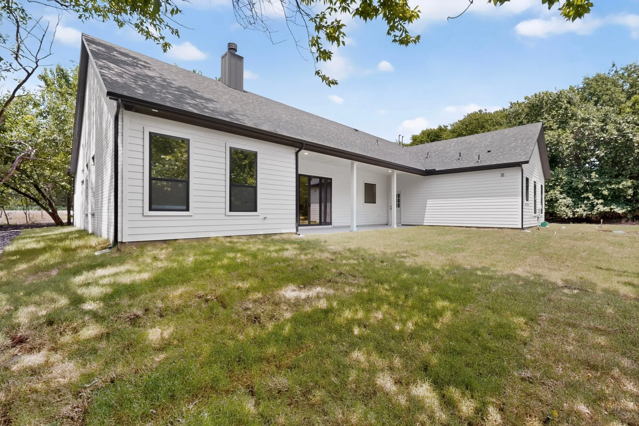 Expansive backyard featuring a white siding exterior with a dark-pitched roof, black-framed windows, and a covered patio area
