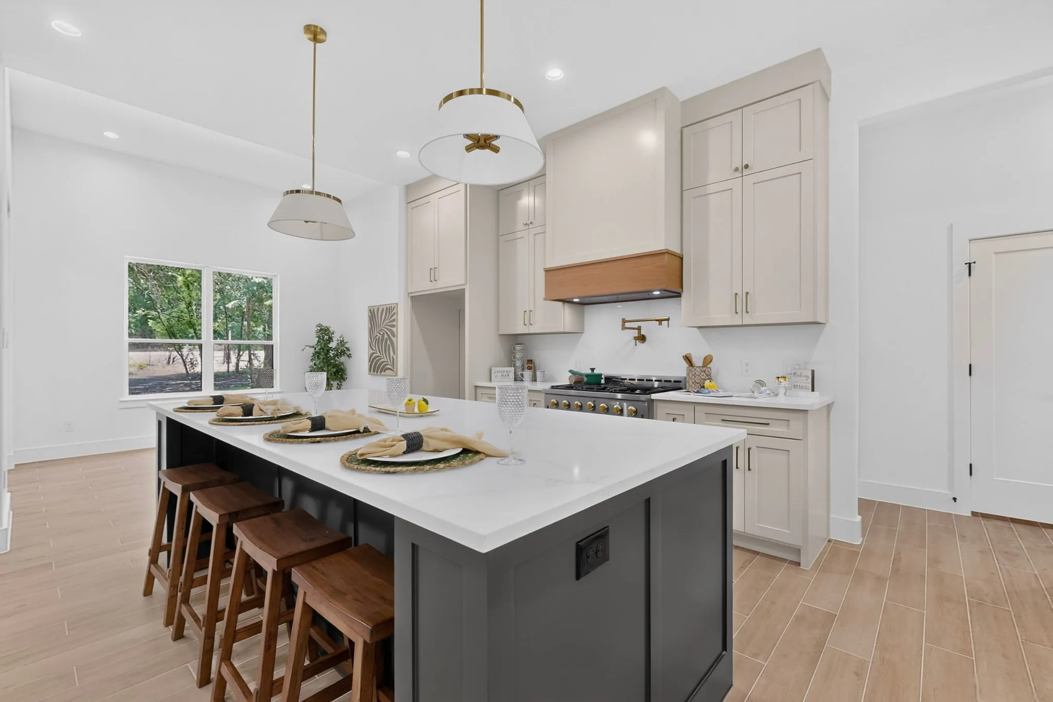 Kitchen featuring a large central island with seating, light-toned cabinetry, a built-in range hood with a wood accent, and wood-finish flooring