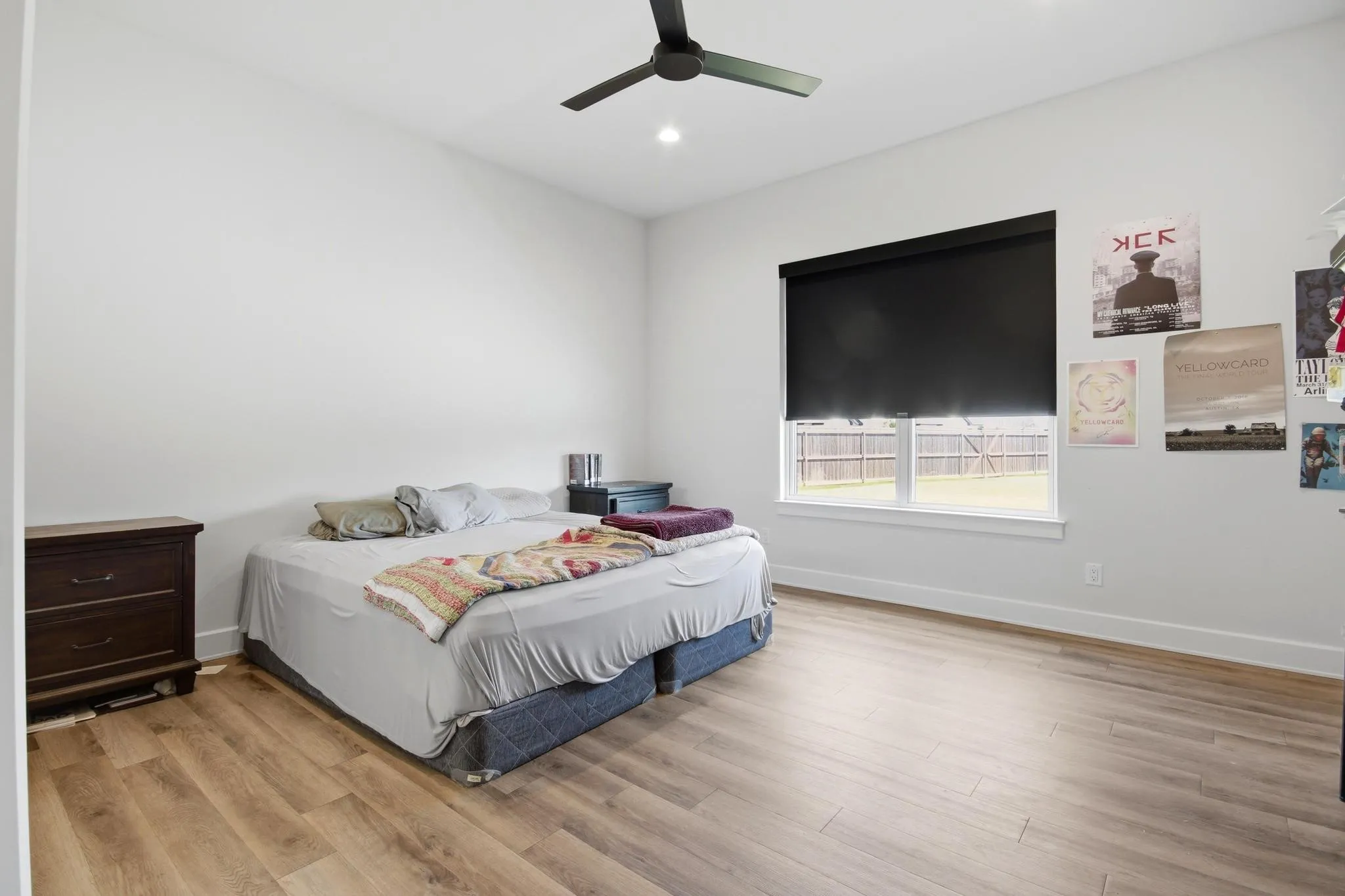Spacious room featuring wood-finish flooring, a large window with a dark roller shade, and a ceiling-mounted fan with integrated lighting