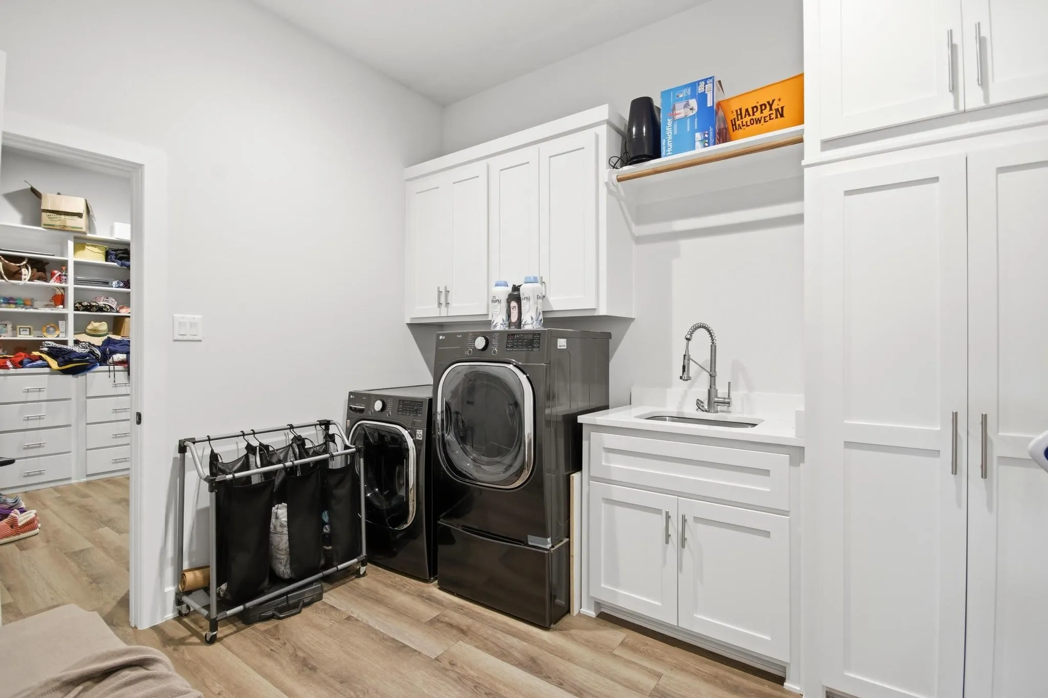 Dedicated laundry area featuring white shaker-style cabinetry, a built-in sink with a pull-down faucet, and wood-finish flooring