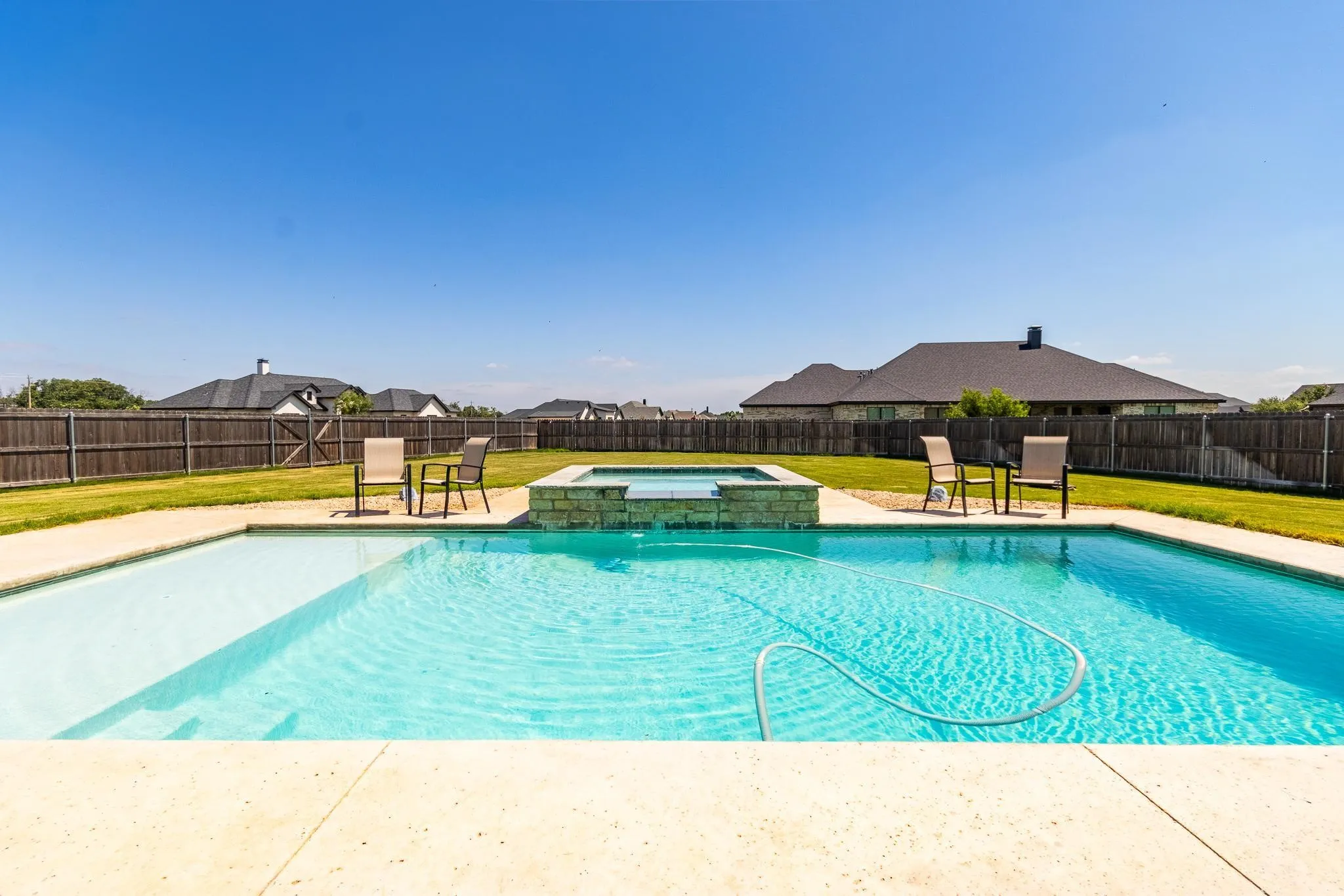 In-ground swimming pool with an integrated spa, surrounded by concrete decking and a grassy yard
