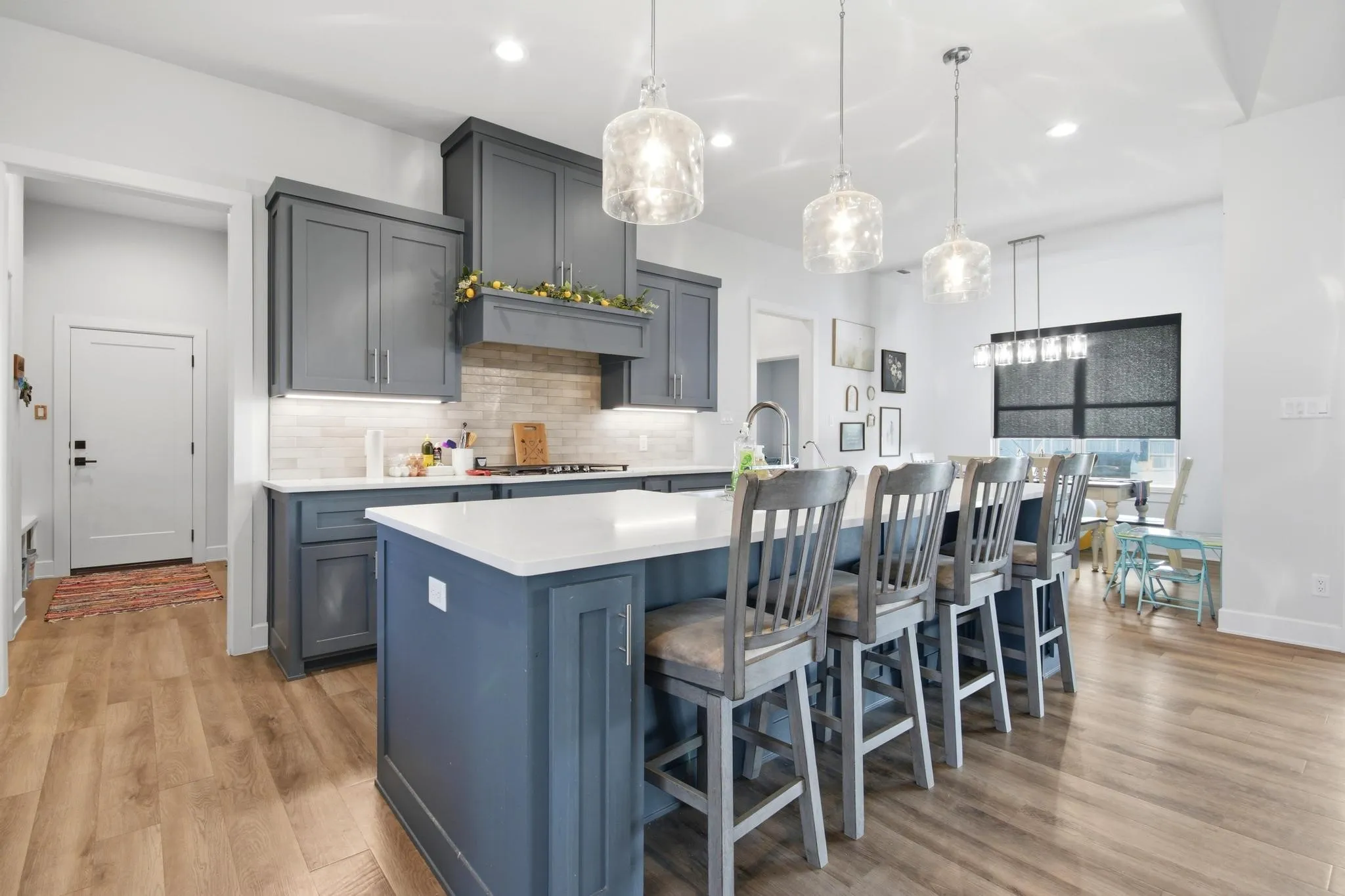 Contemporary kitchen featuring gray shaker cabinetry, a large center island with seating, pendant lighting fixtures, light wood-finish flooring, and a subway tile backsplash