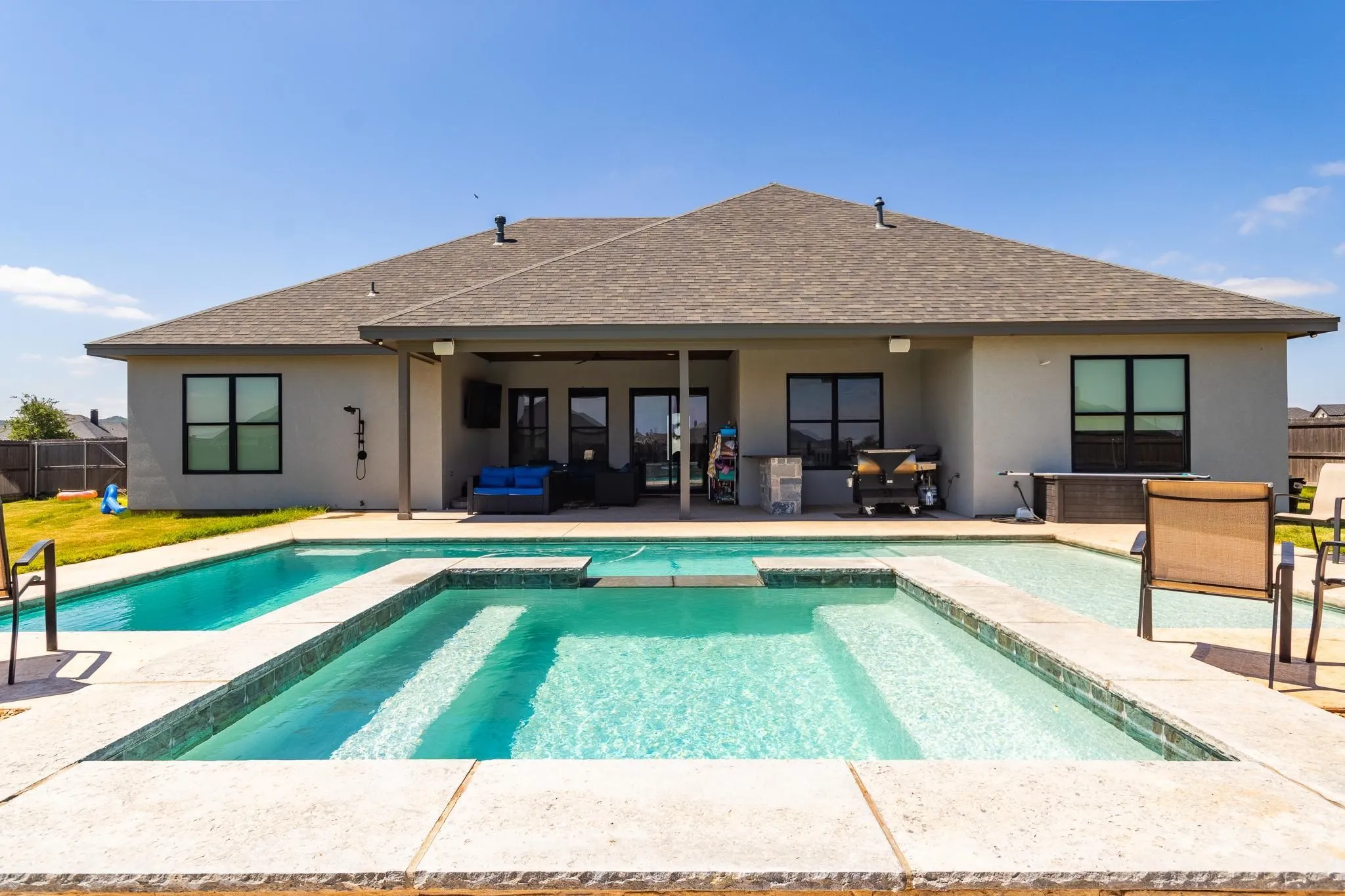 Contemporary stucco exterior with a covered patio, an integrated pool and spa, and a built-in outdoor kitchen